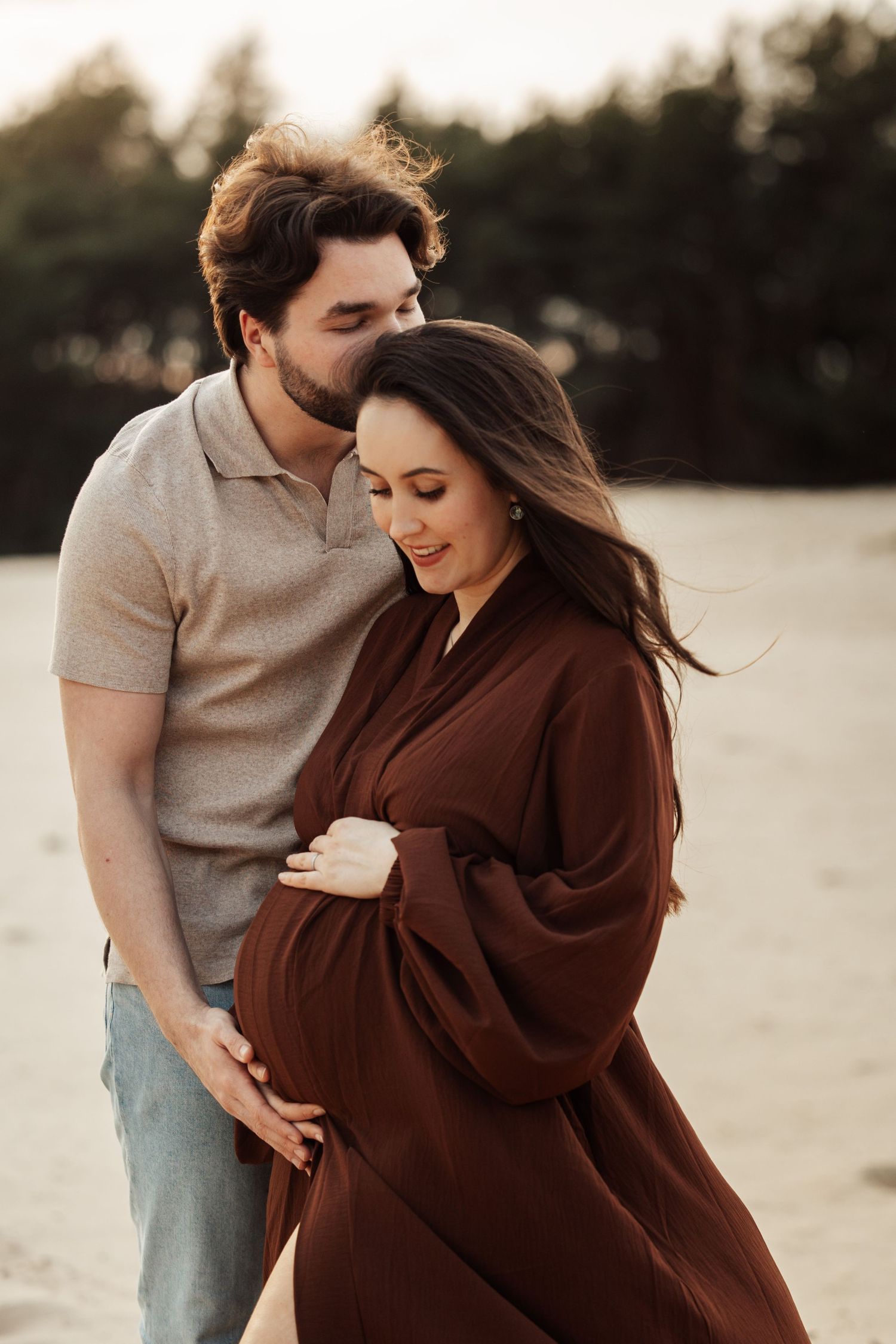 Romantic maternity session featuring couple embracing in brown dress during sunset.