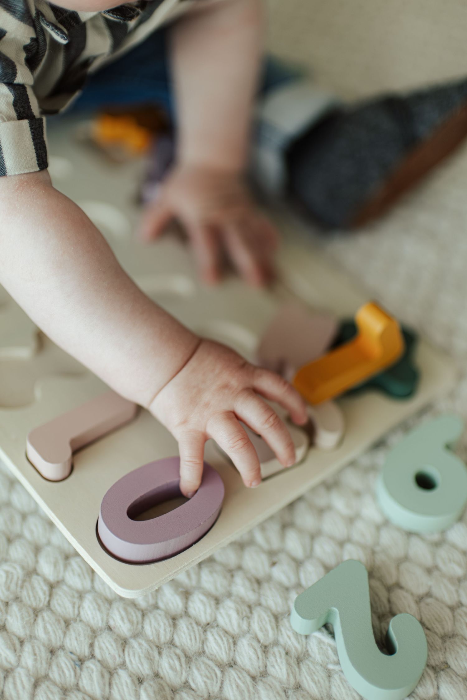 Toddler playing with colorful wooden number puzzle toy on white knit blanket, learning numbers through hands-on play.