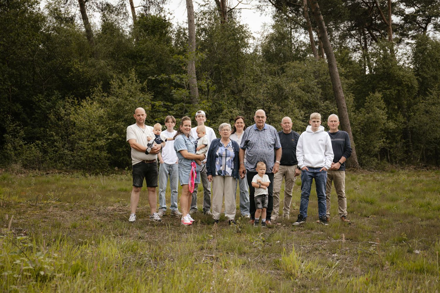 Large family group portrait standing together in a natural woodland clearing surrounded by trees.