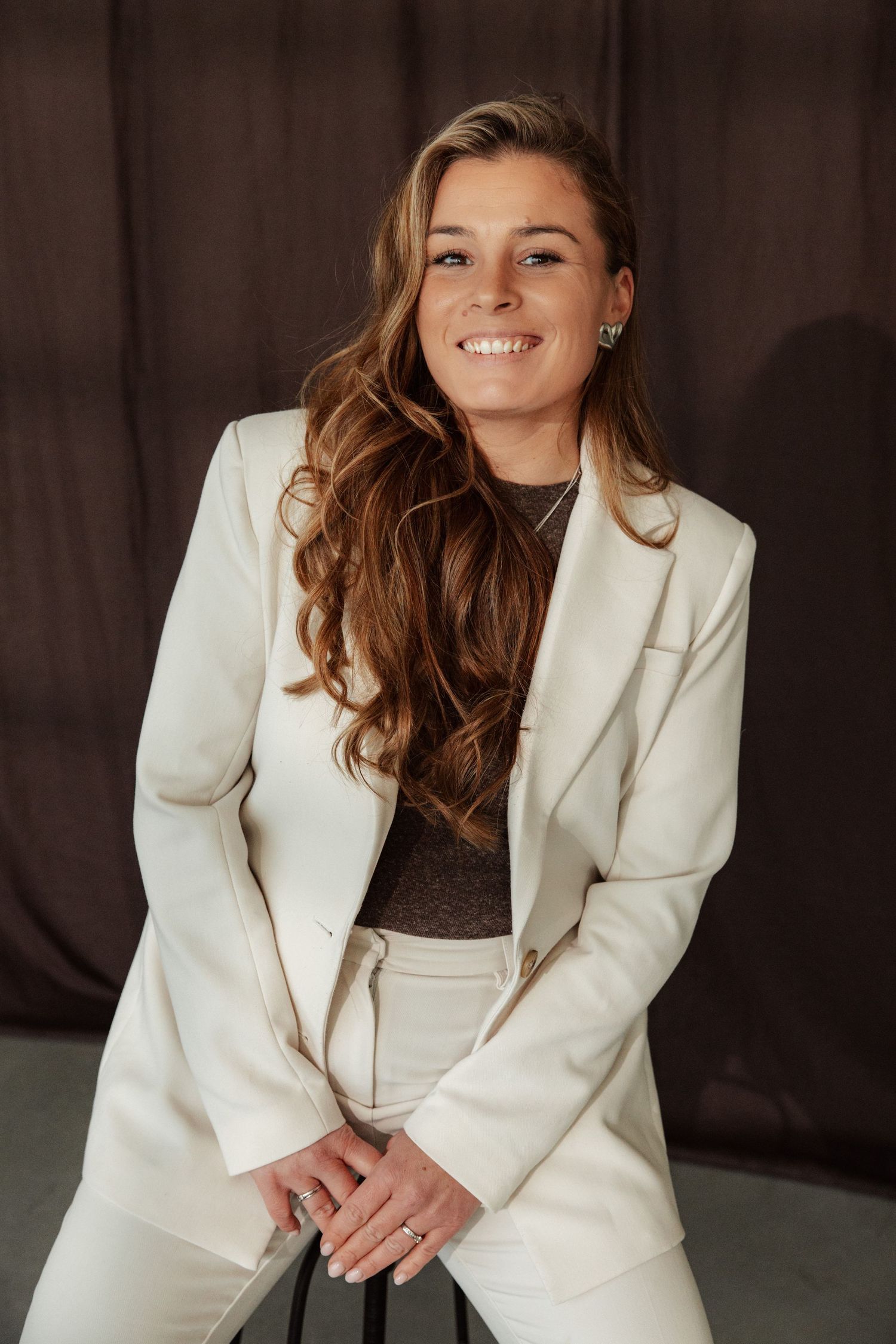 Professional portrait of a person in a white blazer suit against a dark background.