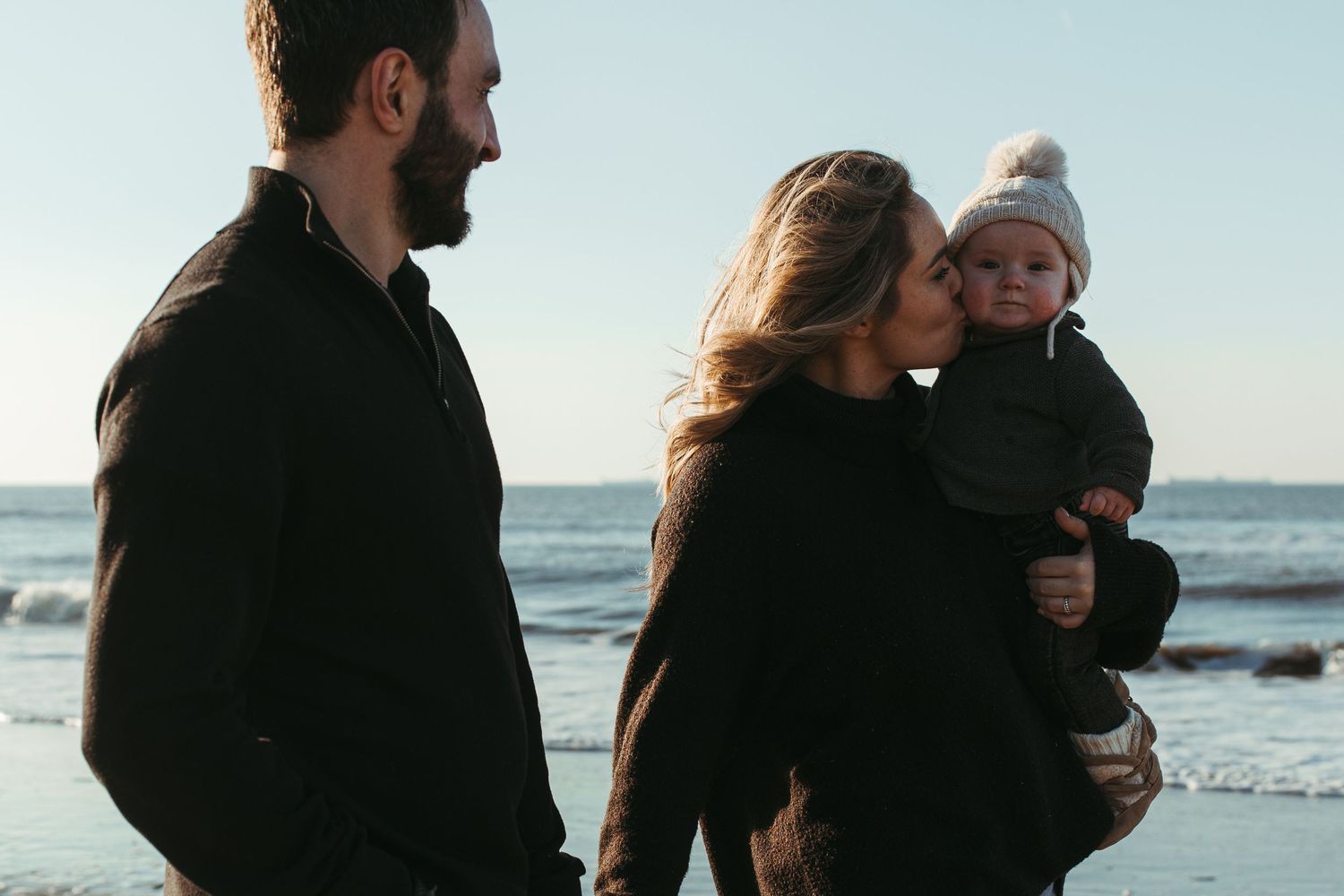 A family moment captured at sunset on a beach with waves in the background.