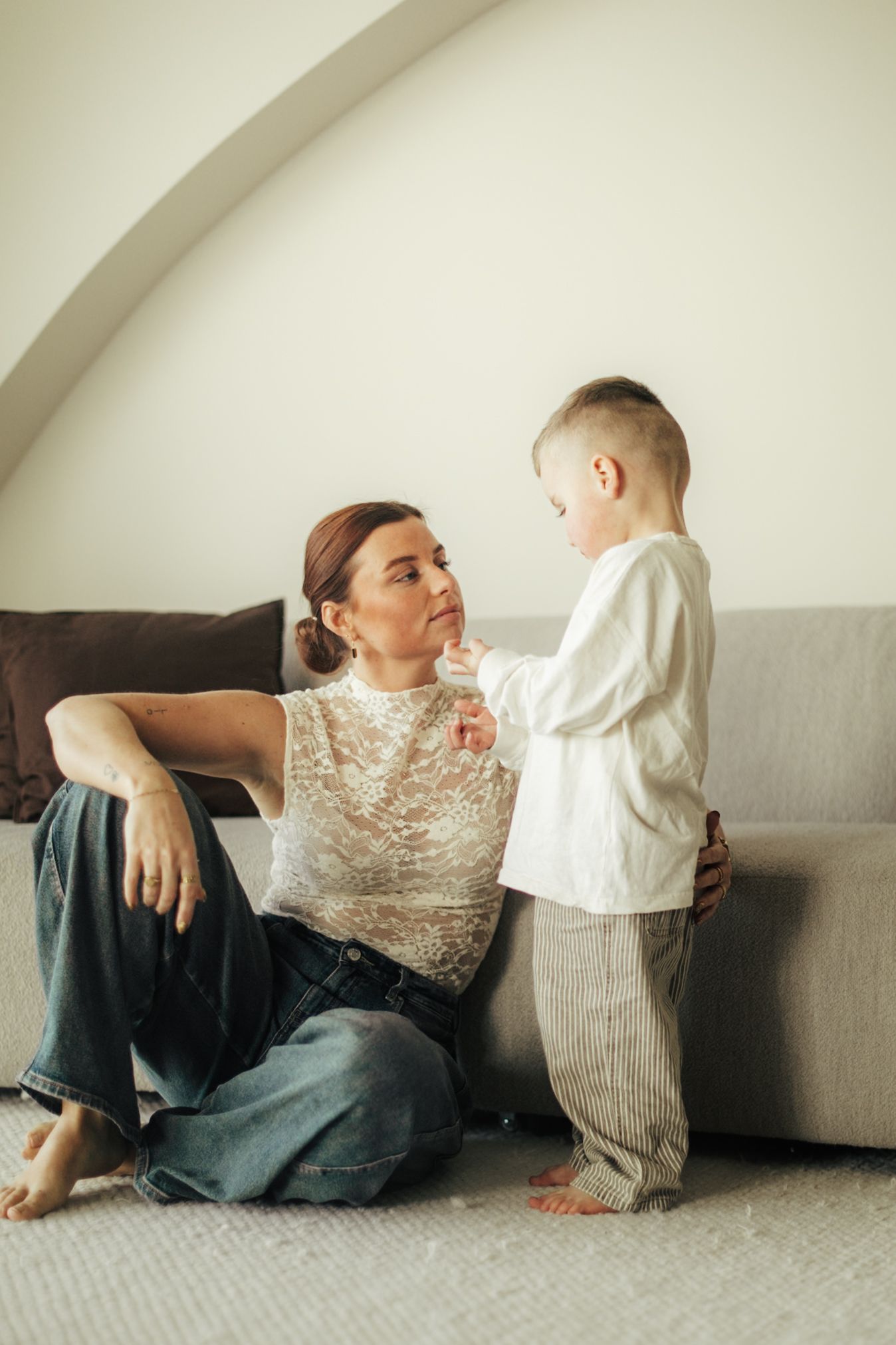 Casual indoor portrait of parent and child having conversation on grey sofa.
