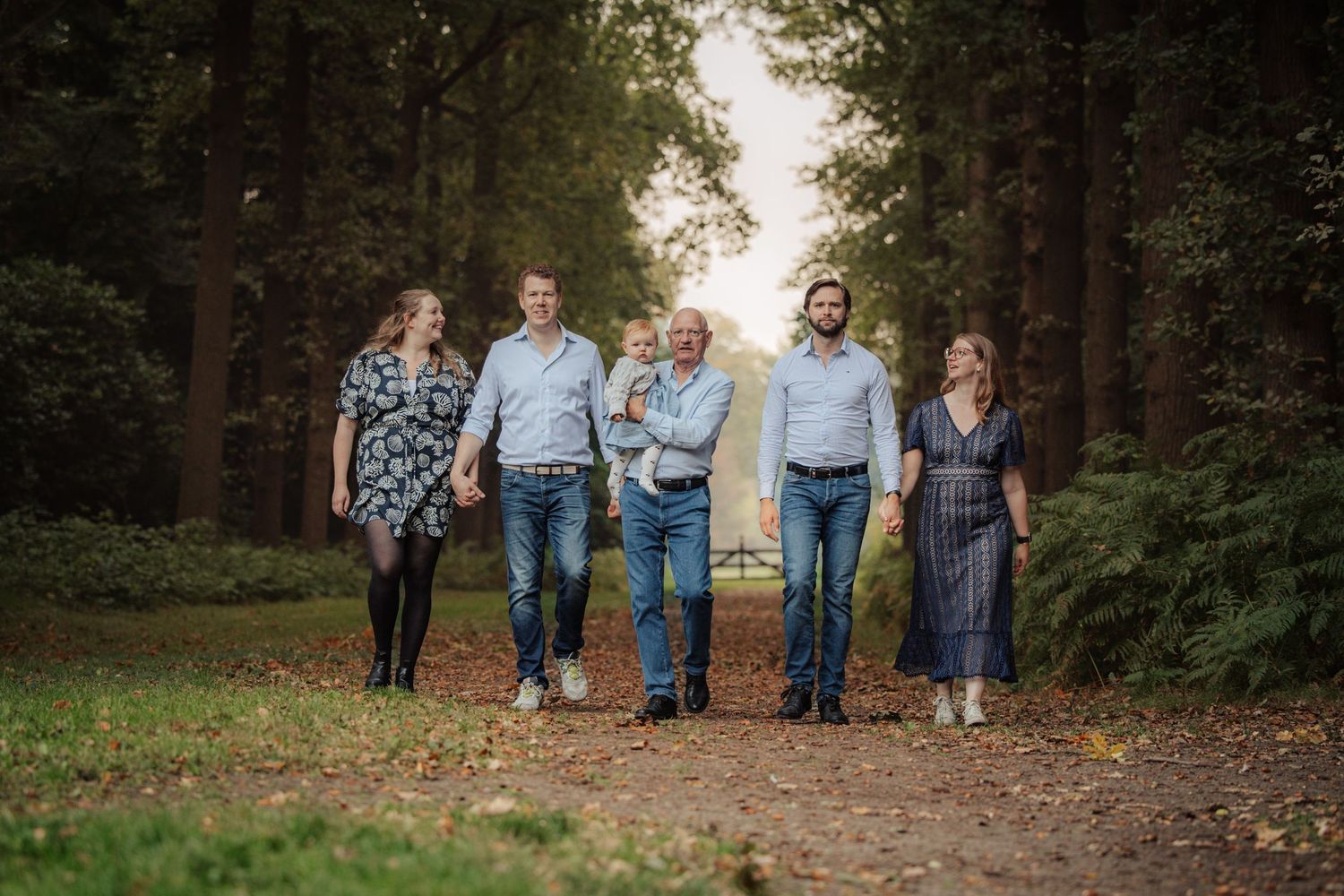 Family walking together on a tree-lined autumn path.