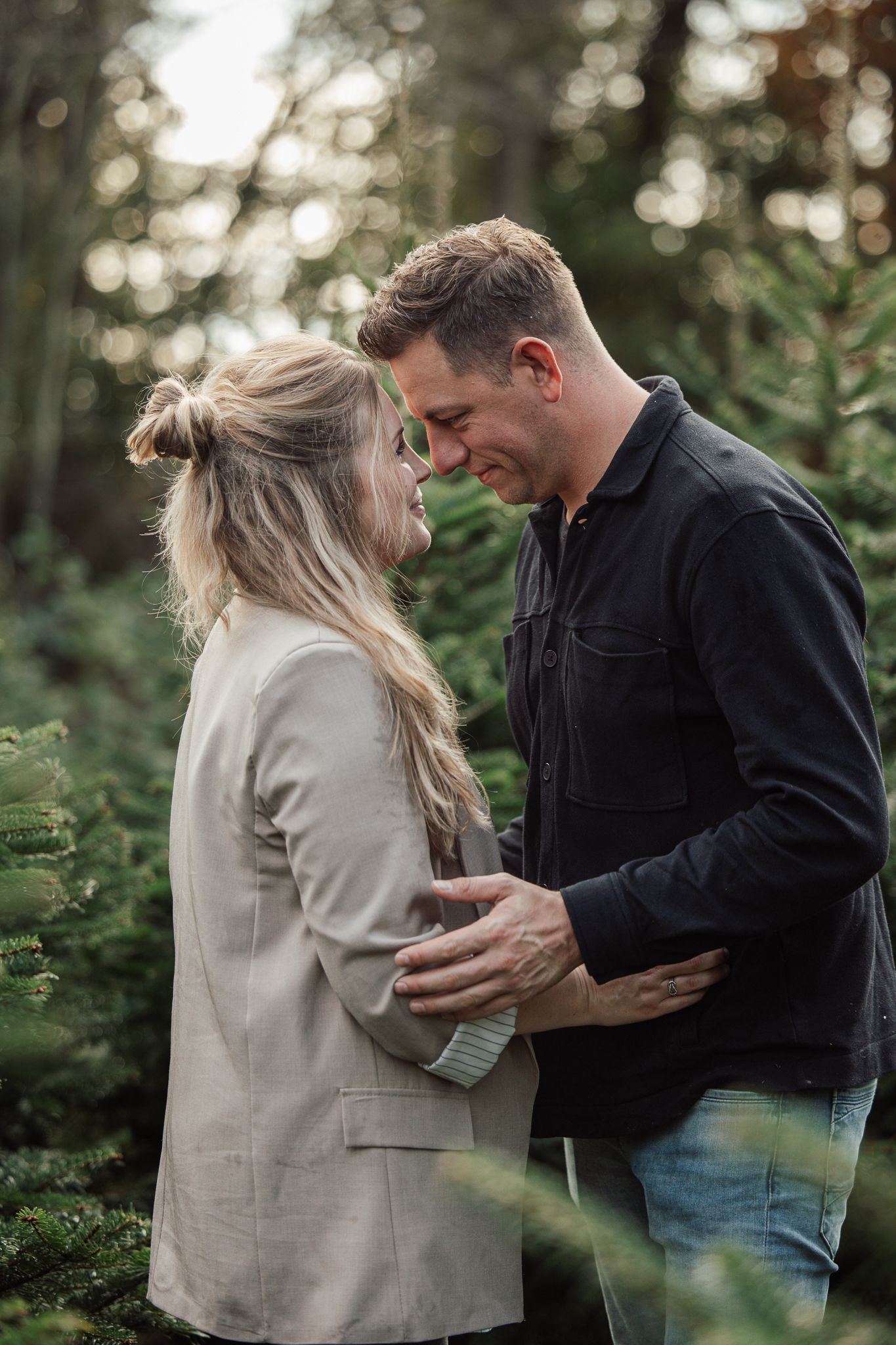 Couple sharing emotional moment between pine trees at a Christmas tree farm.