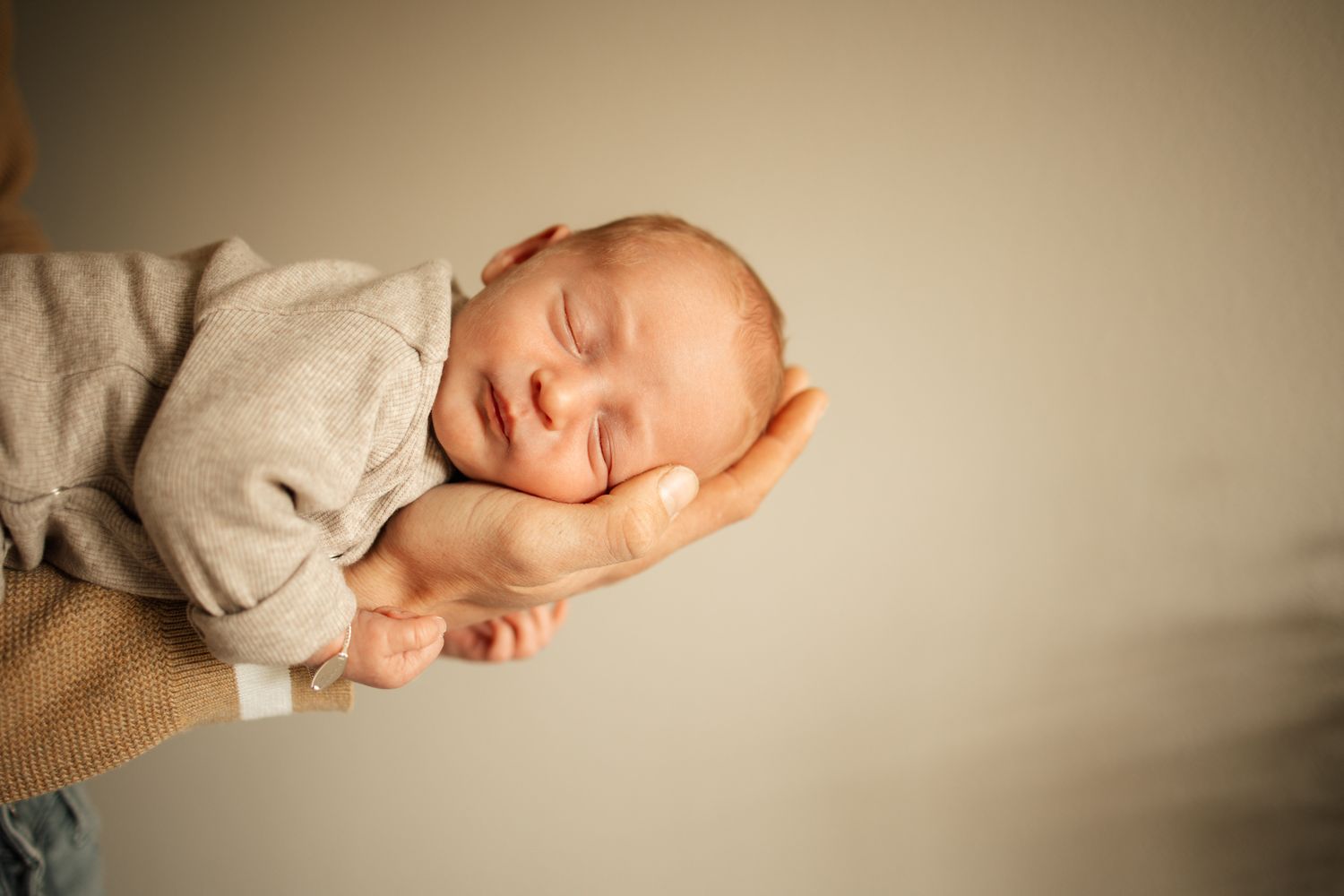 Peaceful sleeping newborn photographed against neutral background.