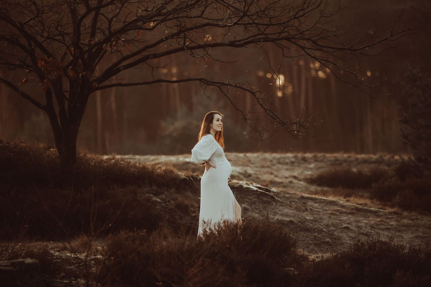 A couple stands in a golden field at sunset wearing white clothing.