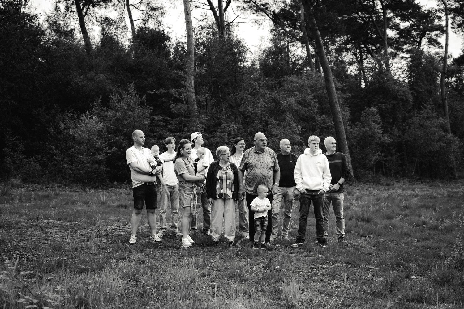 Black and white photo of a large family group posing together in a grassy field with trees in the background.