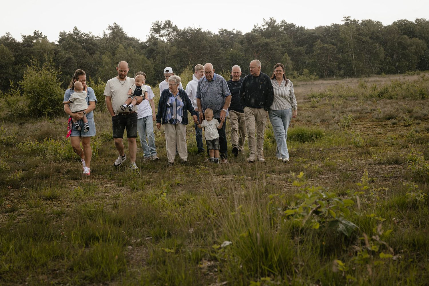 A multigenerational family group poses together in an open field with trees in the background.