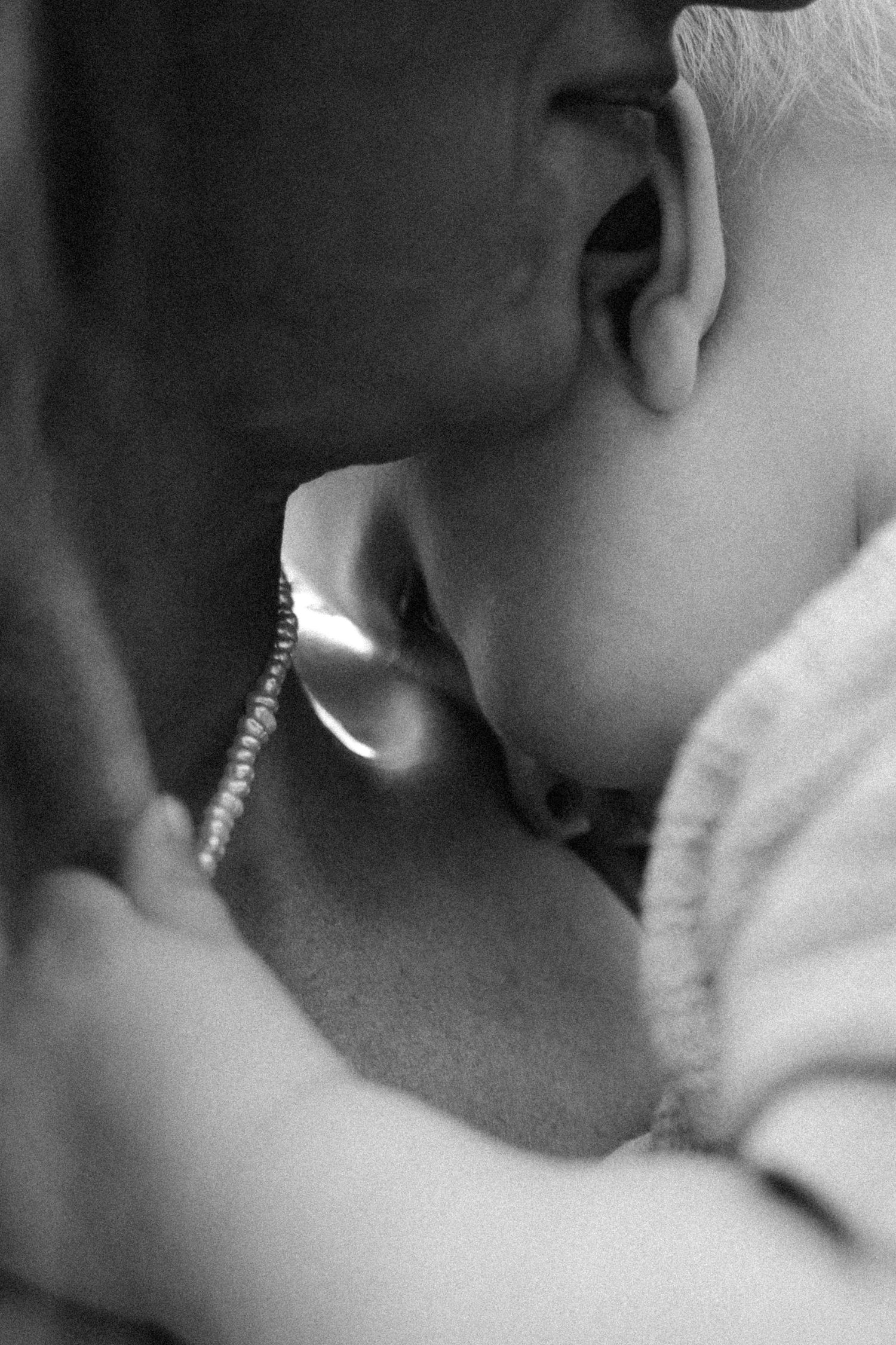 Black and white close-up of a baby chewing on a silver spoon, wearing a soft knit sweater.