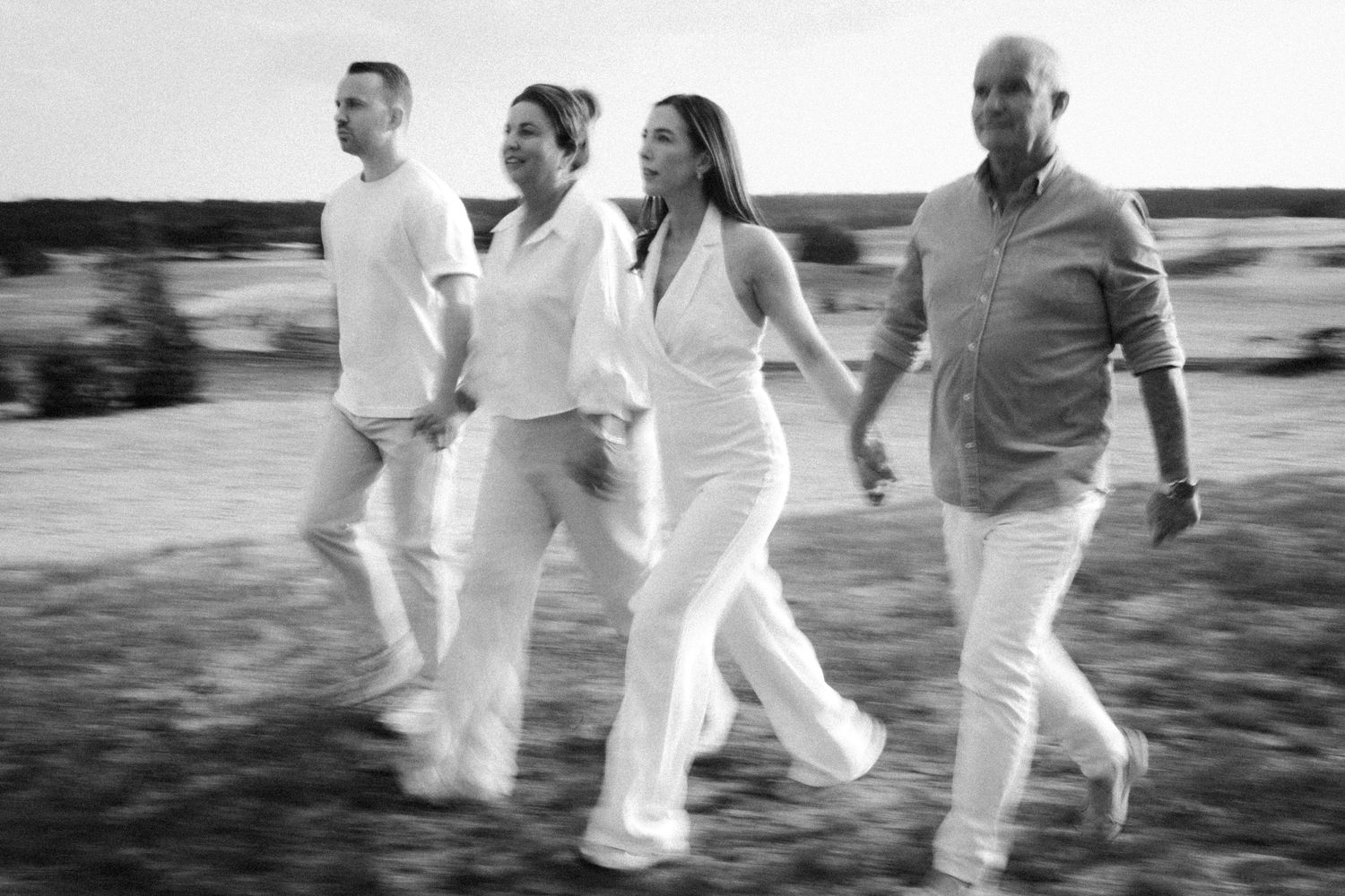 Black and white photo of four people walking together across an open field in white outfits.