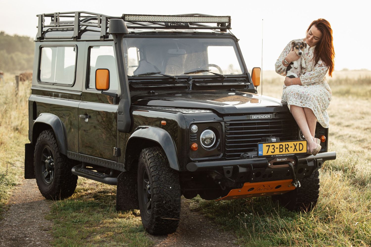 A vintage Land Rover Defender parked on grassy terrain during a sunset photoshoot.
