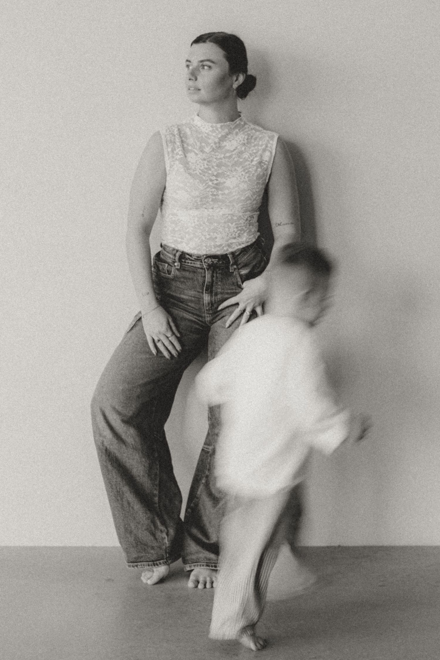 Black and white portrait showing figure in lace top and jeans with blurred motion in foreground.