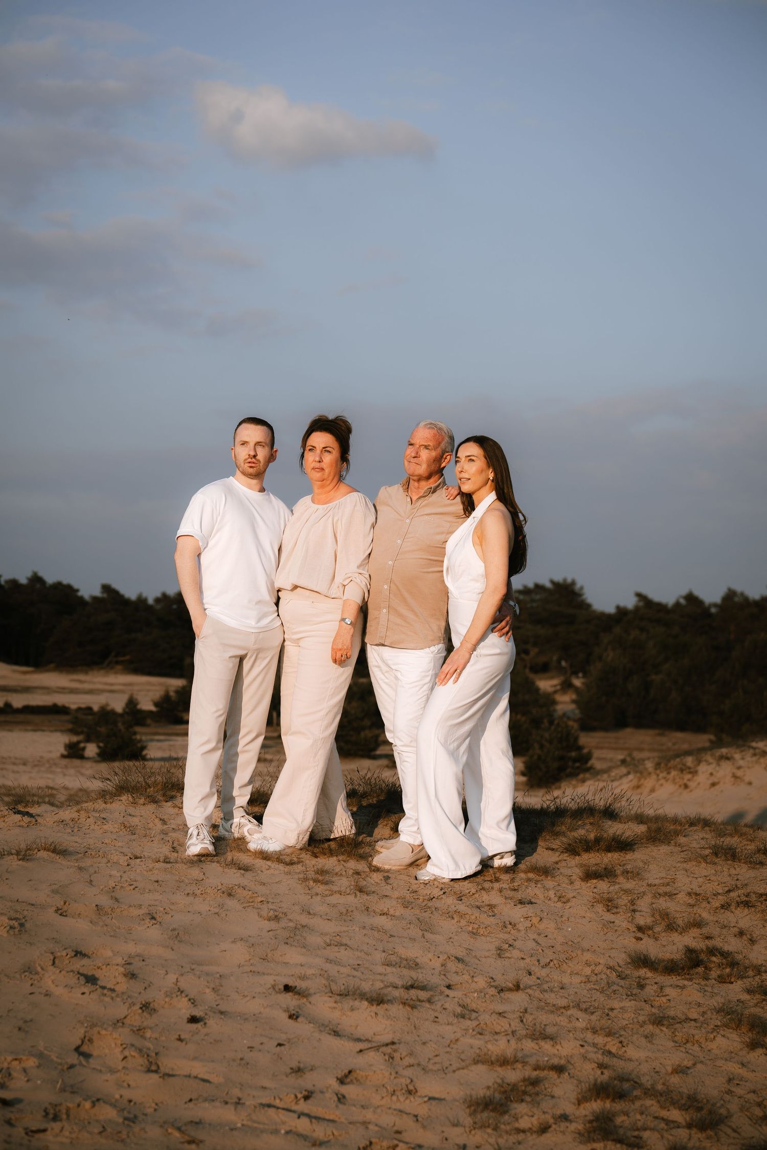 Family of four posing together on sandy beach during golden hour sunset.