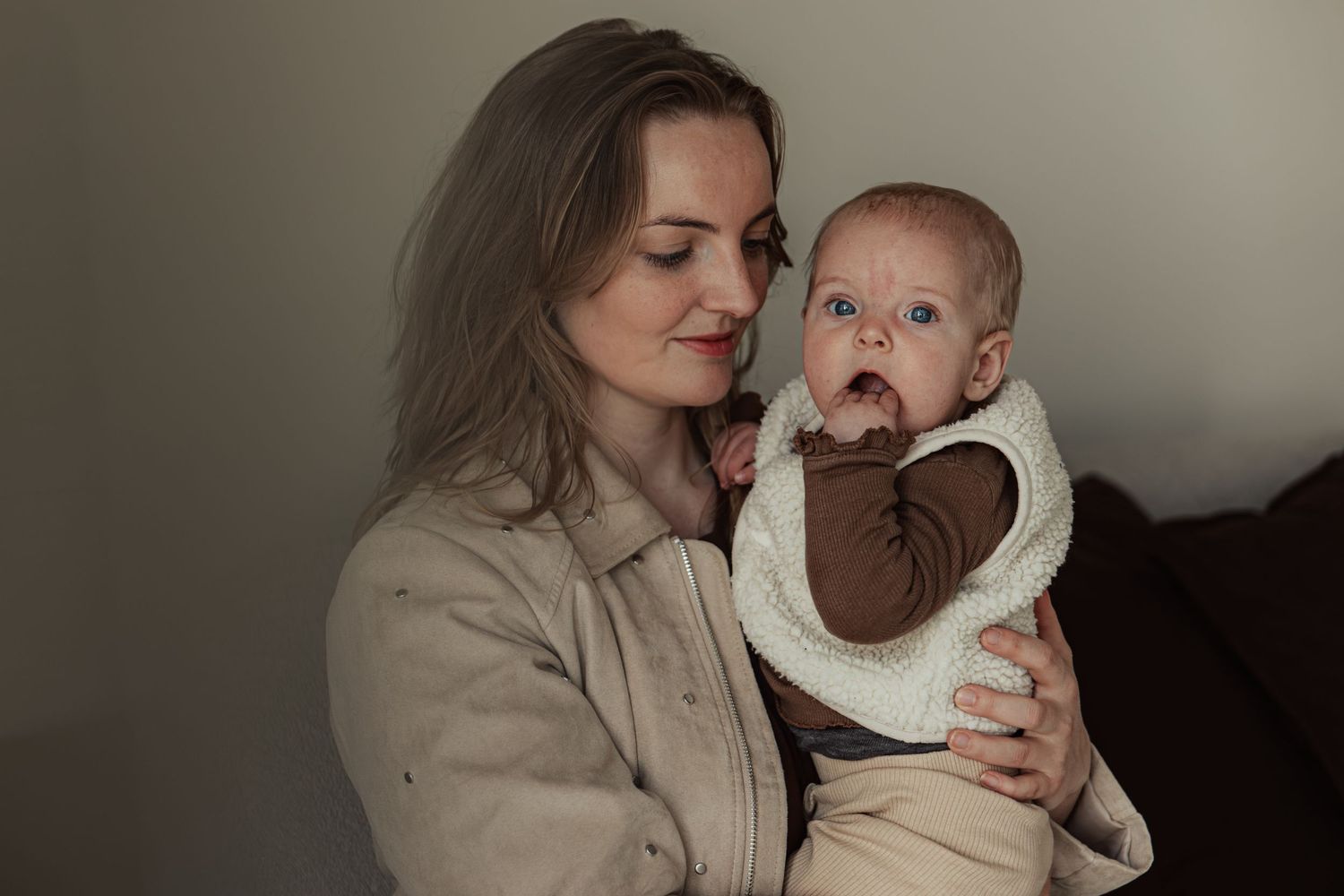 A young mother tenderly holds her blue-eyed baby dressed in a brown outfit with white bib.