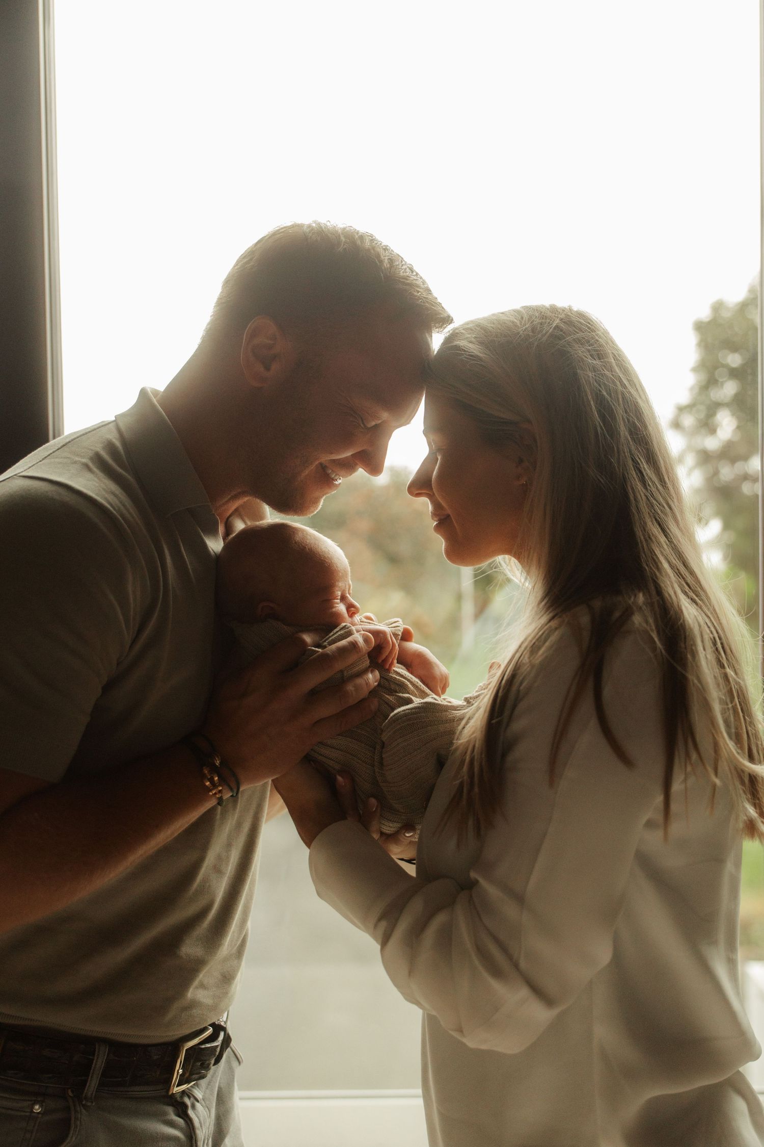 Intimate silhouette portrait against window light in tender embrace.