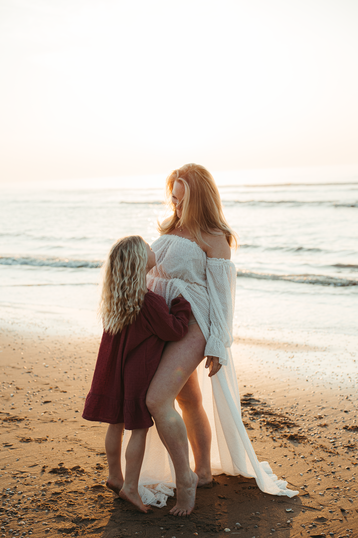 Intimate beach scene with two figures embracing by the ocean at sunset.