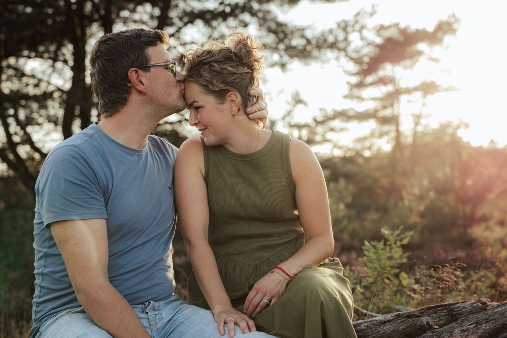 A couple embraces while sitting outdoors among pine trees at dusk.