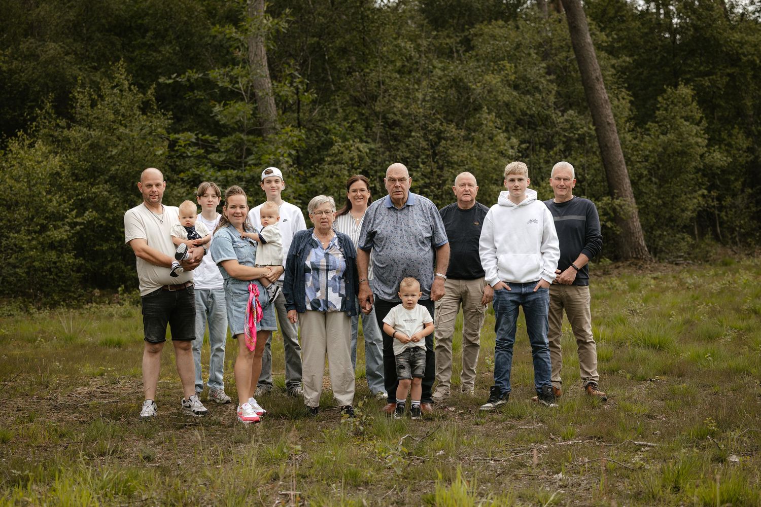 Large family group posing together outdoors in a forest clearing, spanning multiple generations including children and elderly adults.