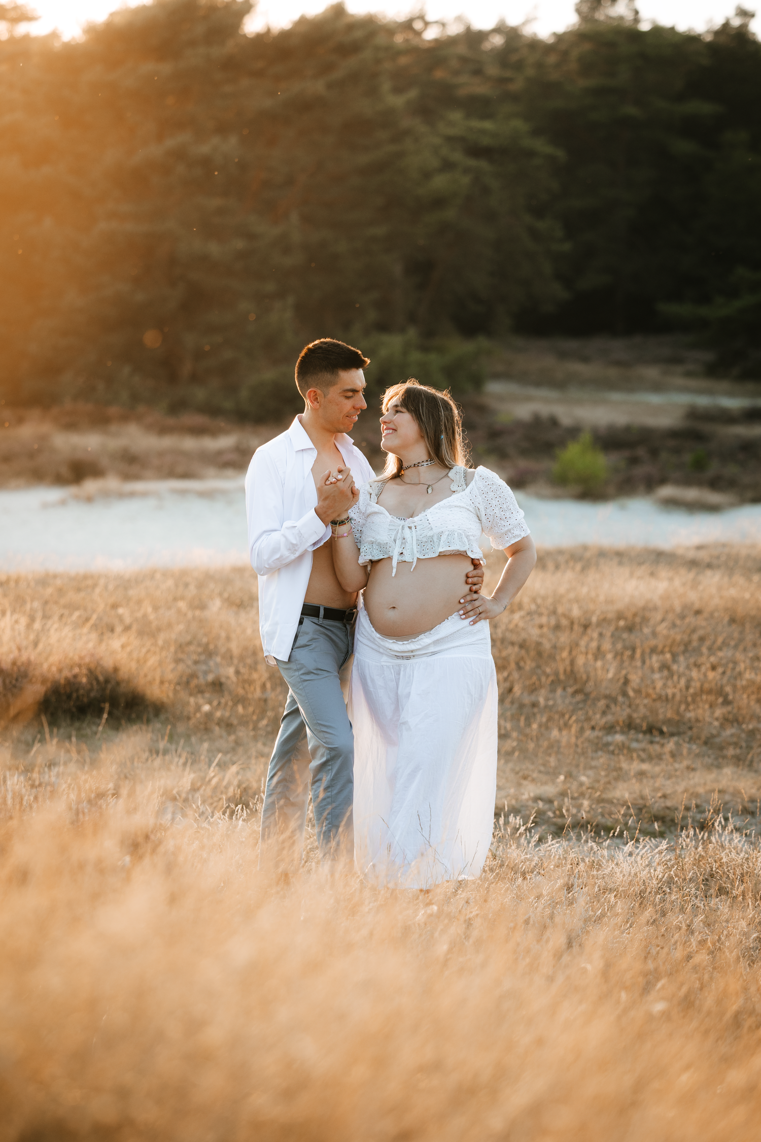 A couple shares an intimate moment in a golden field at sunset during a maternity photoshoot.