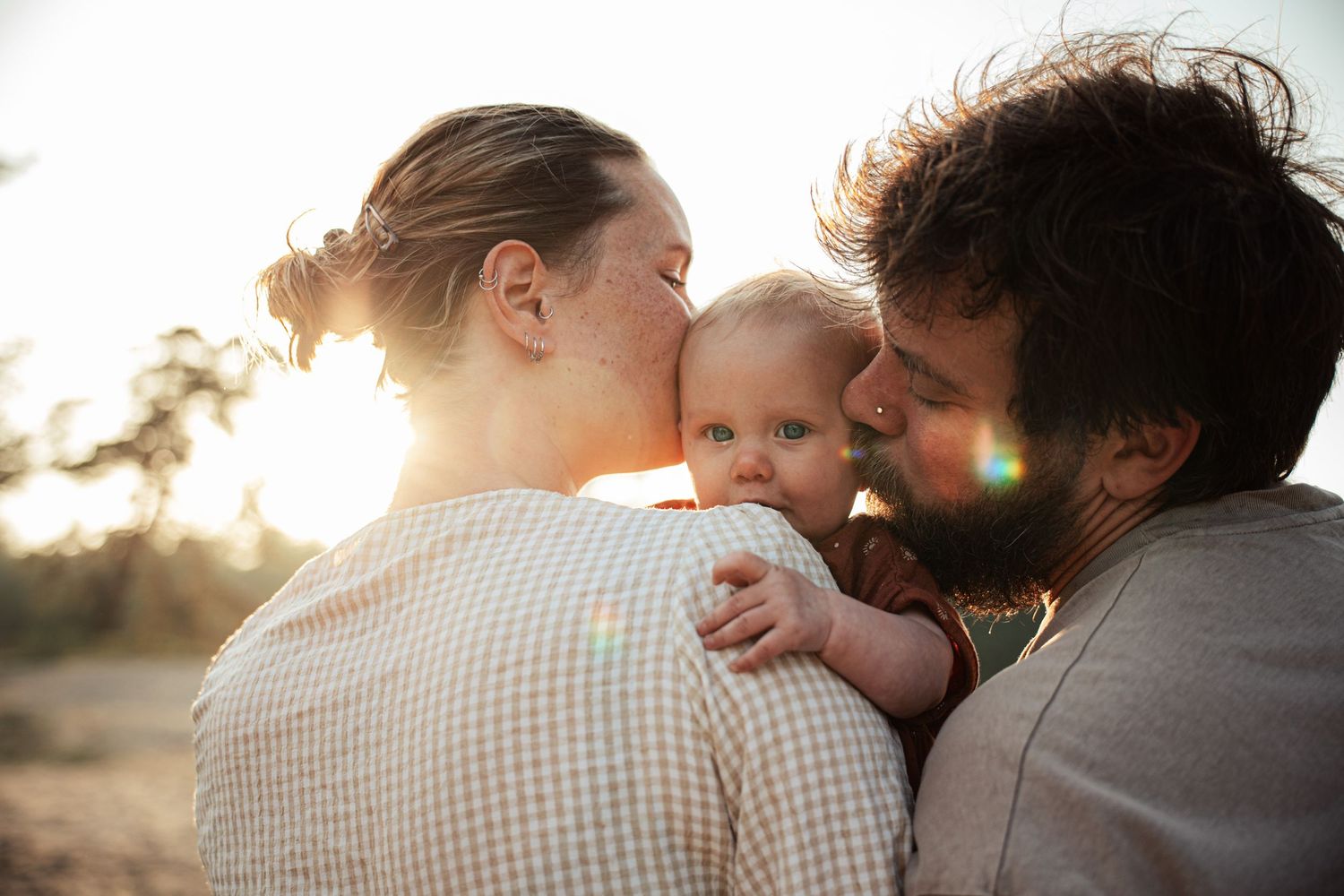Intimate family portrait captured during golden hour with sun flare.