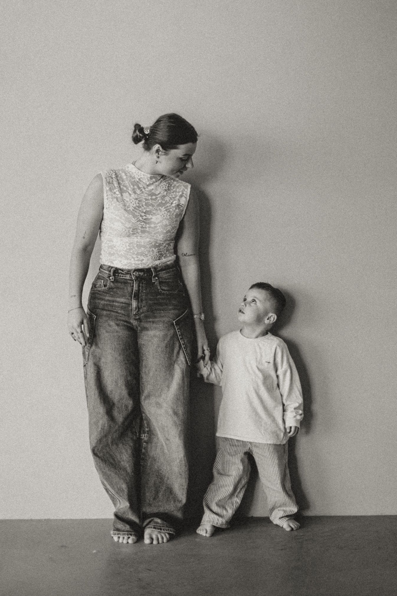 Artistic black and white series showing parent and child standing against wall in denim.