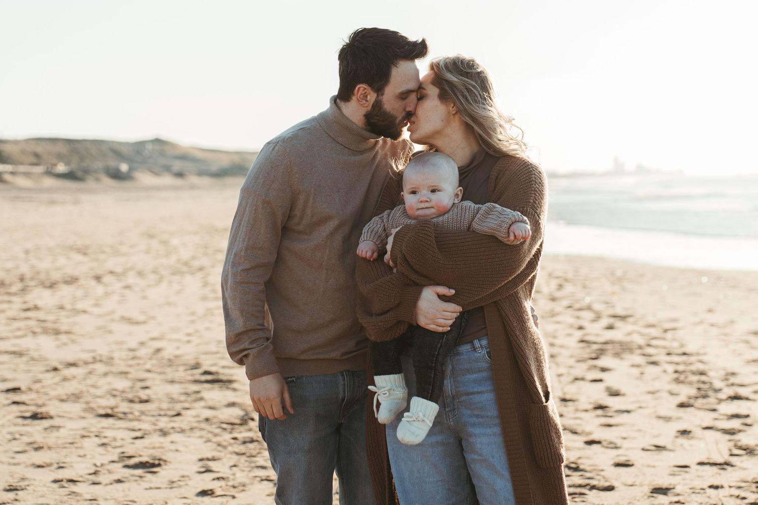 A tender family embrace on a sandy beach during golden hour.