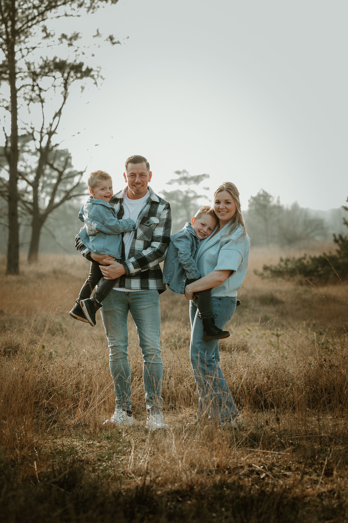 Family of four poses together in casual attire against misty forest backdrop.
