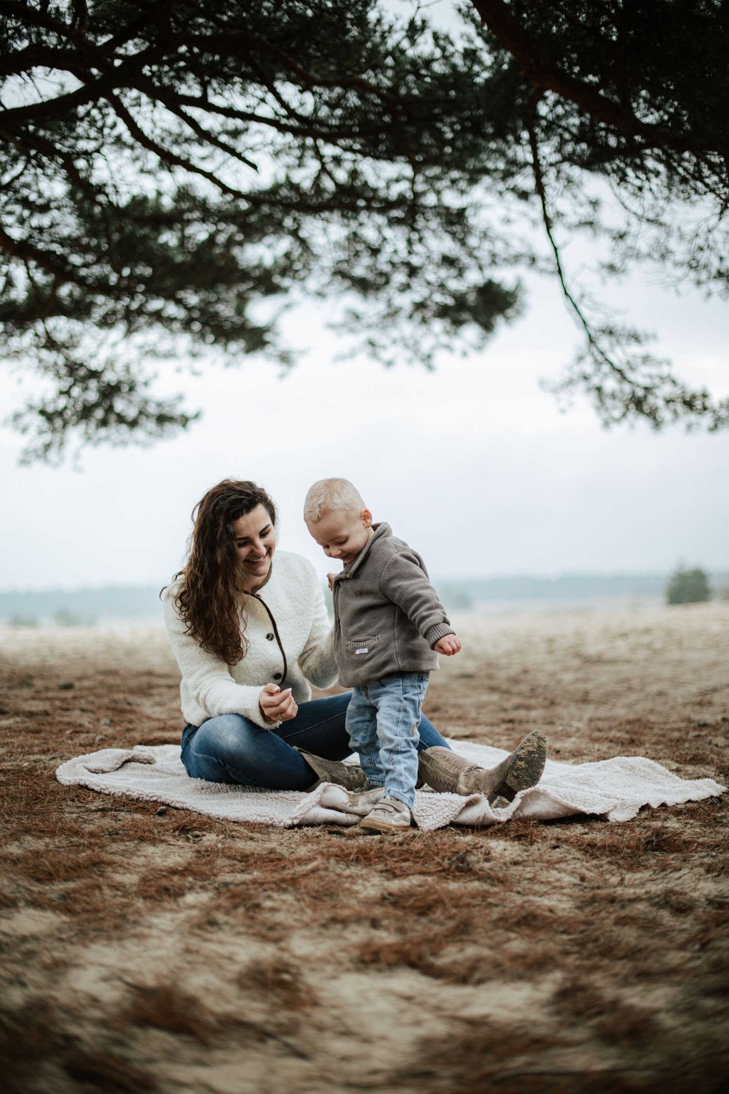 Family relaxing on blanket under pine trees during casual outdoor photoshoot.