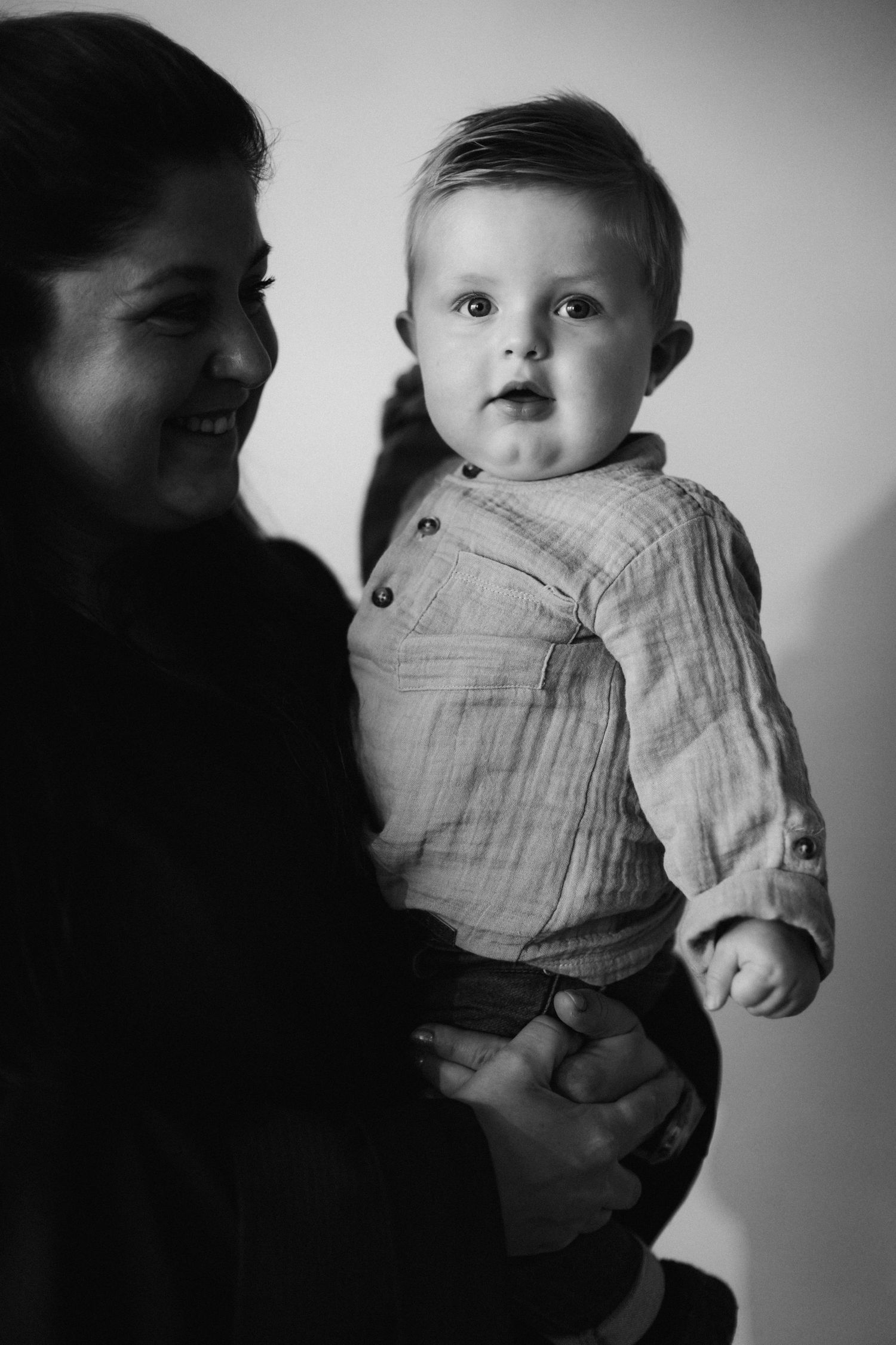 Black and white photo of a smiling mother holding her curious baby boy in a button-up shirt.