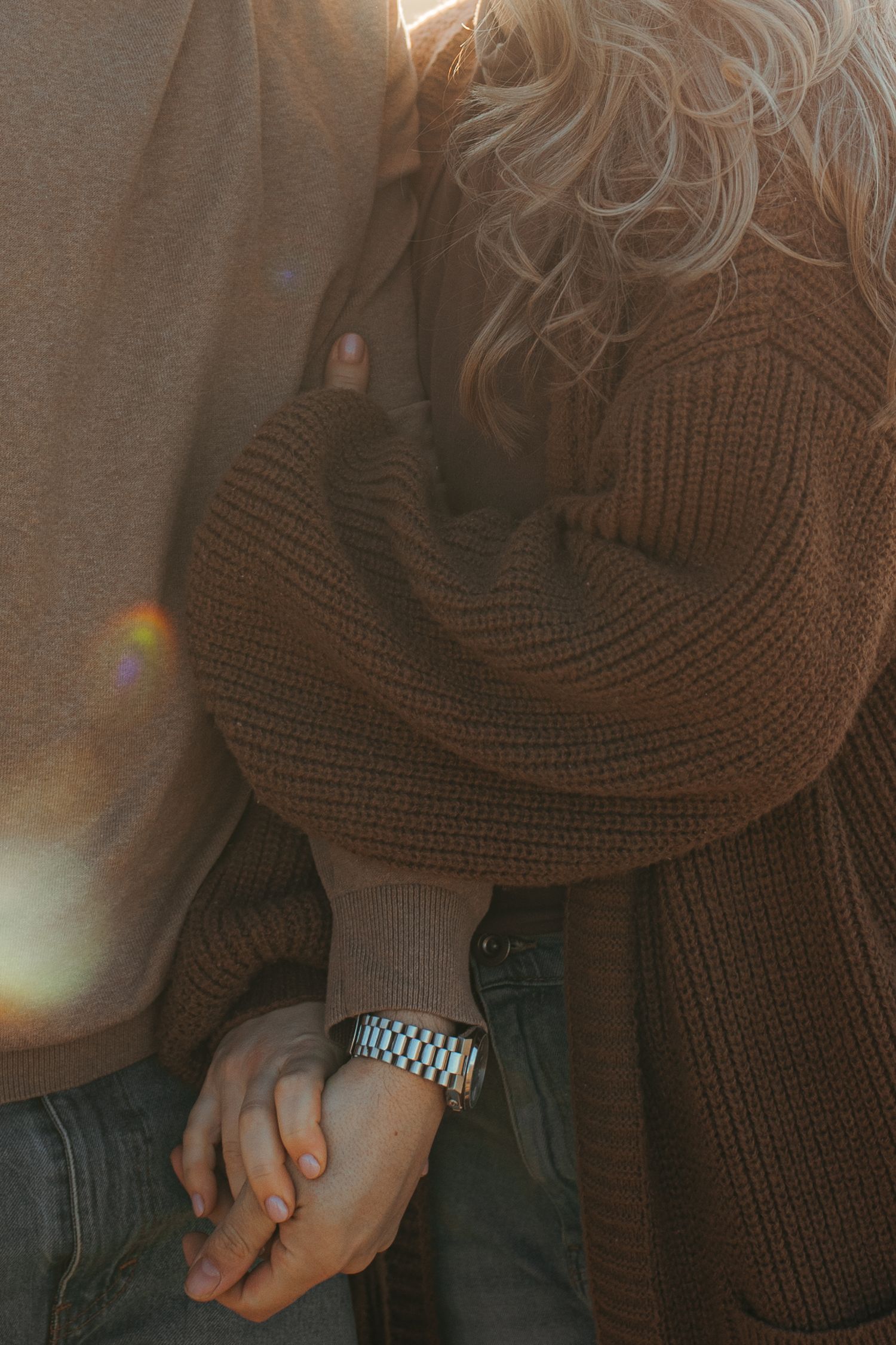 Close-up detail of hands clasped together wearing a brown knit sweater and watch.