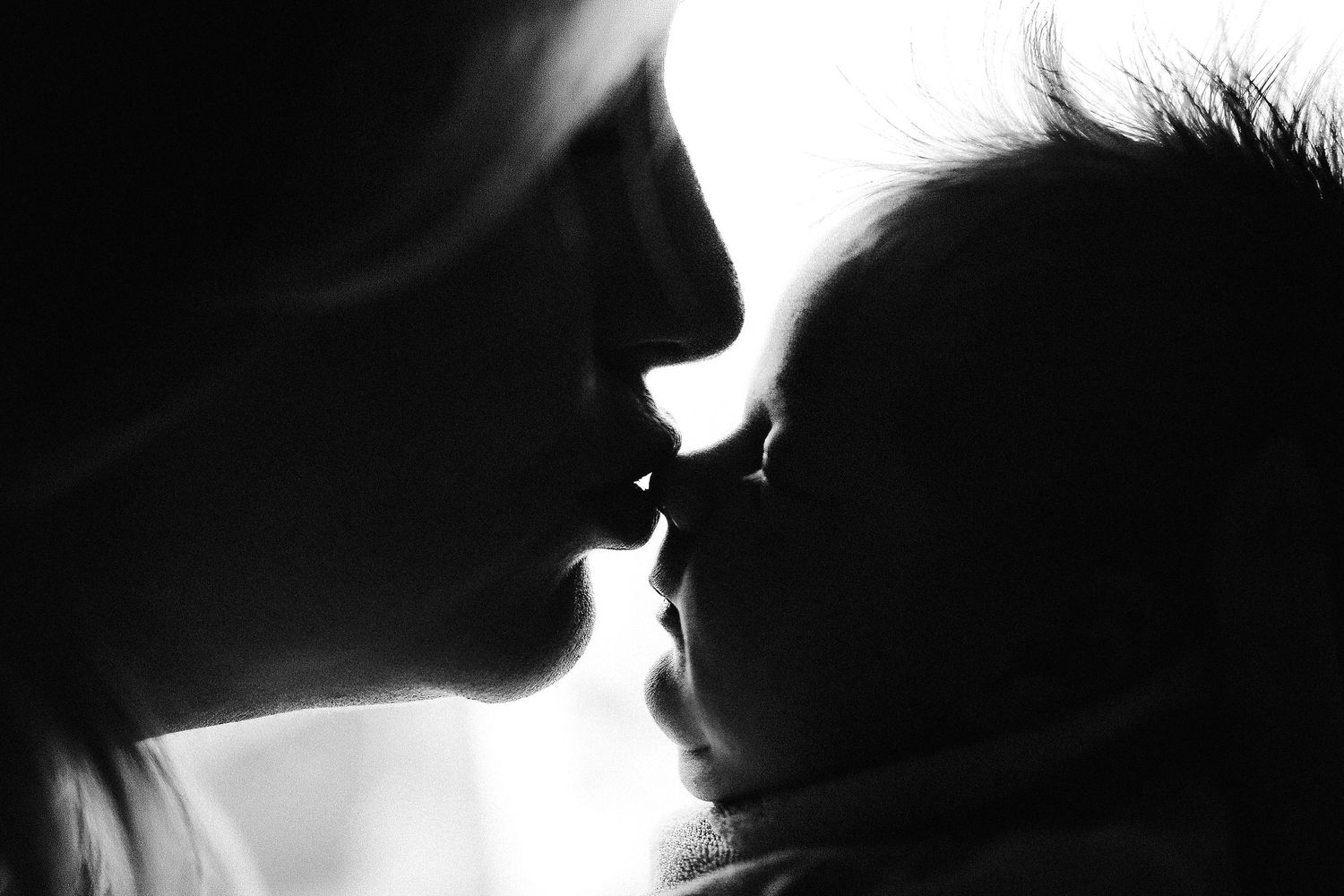 Black and white silhouette of a mother gently kissing her newborn baby, capturing a tender bonding moment.