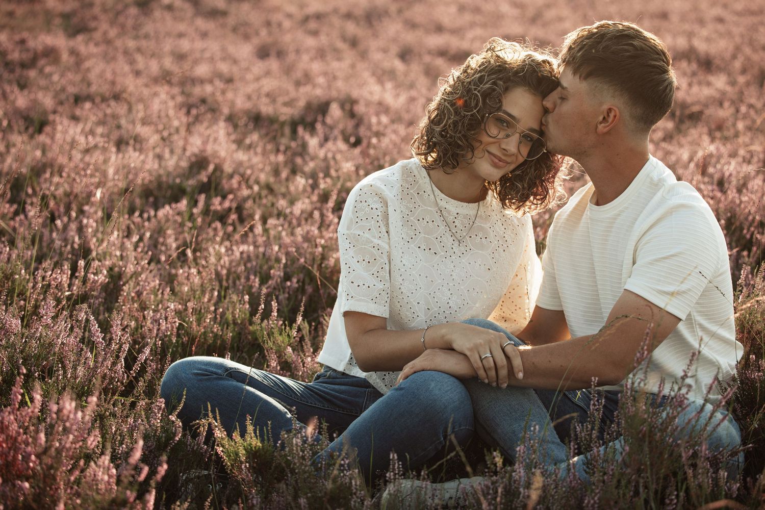 Couple sharing an intimate moment in a field of heather during golden hour sunset.