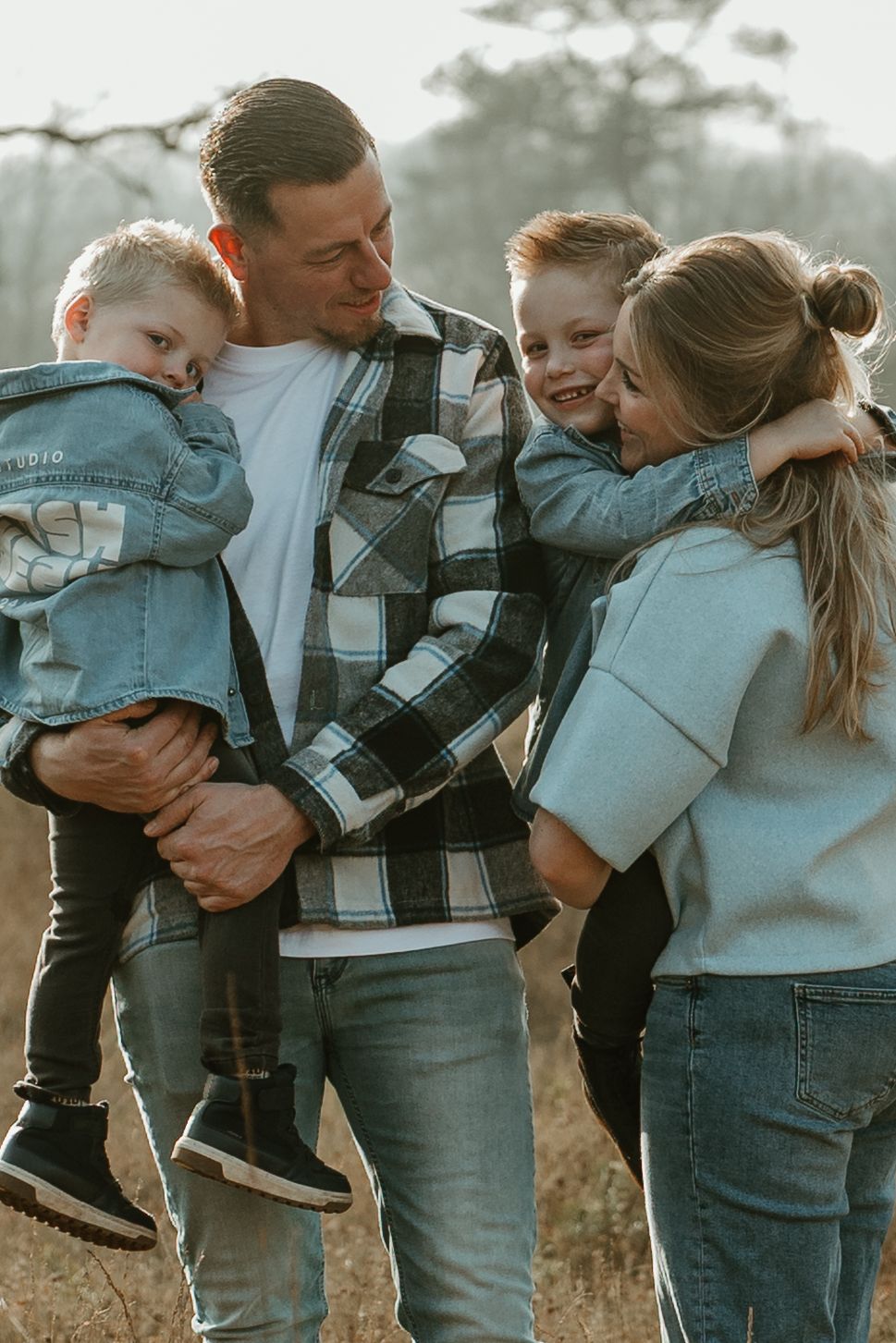 A loving family shares an intimate moment together outdoors during golden hour while wearing casual denim and plaid.