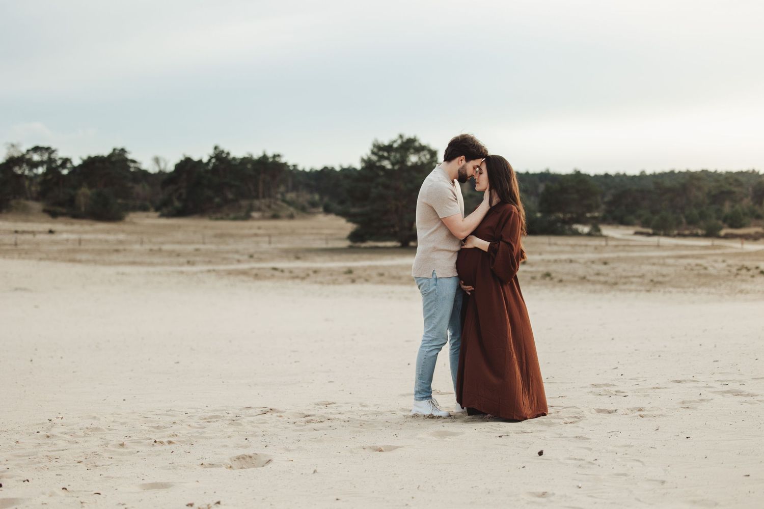 Couple sharing tender moment during outdoor maternity photoshoot on sandy beach.