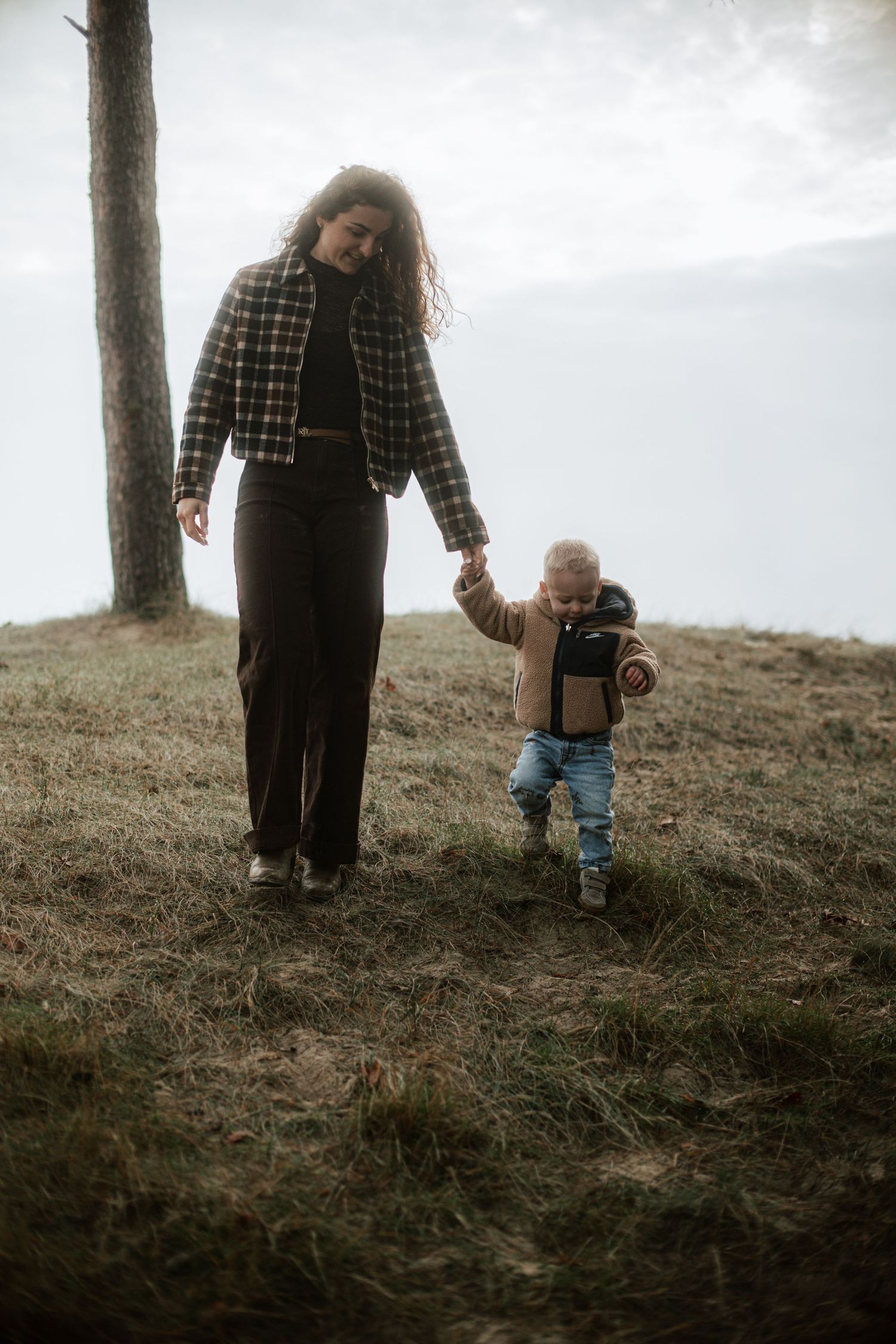 Adult and small child walking together on a grassy hillside during an outdoor photo session.
