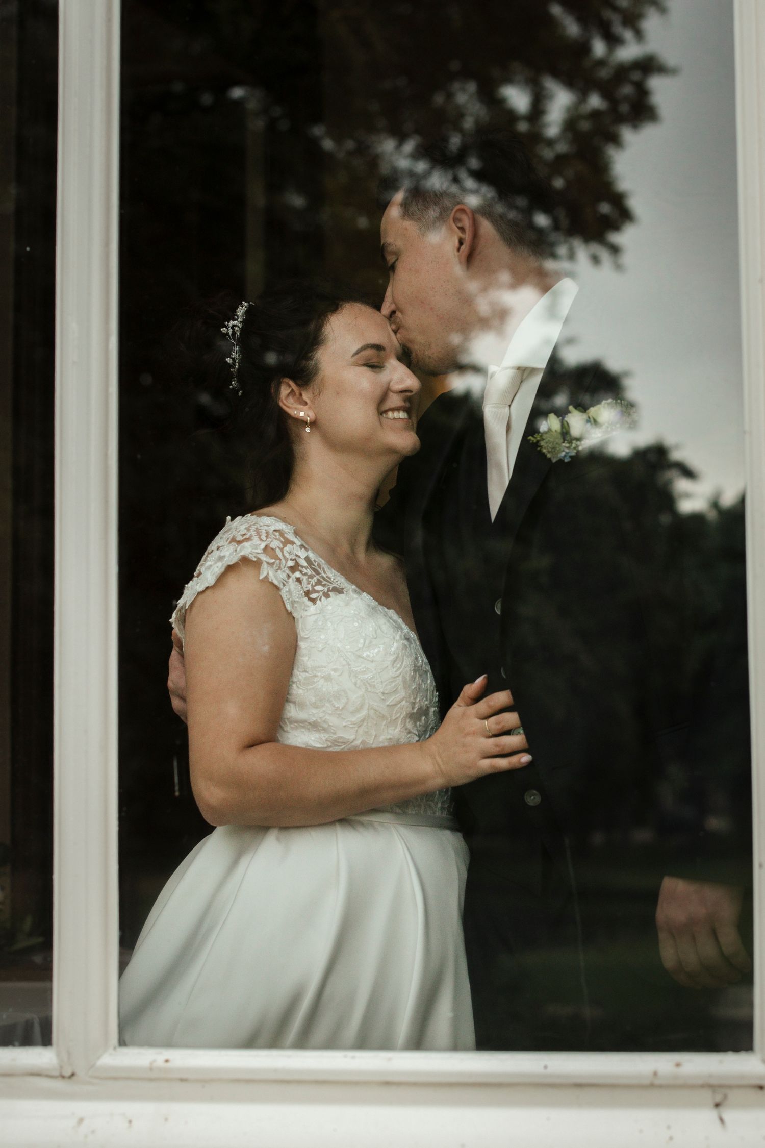 Romantic wedding moment captured through window reflection showing couple in elegant attire.