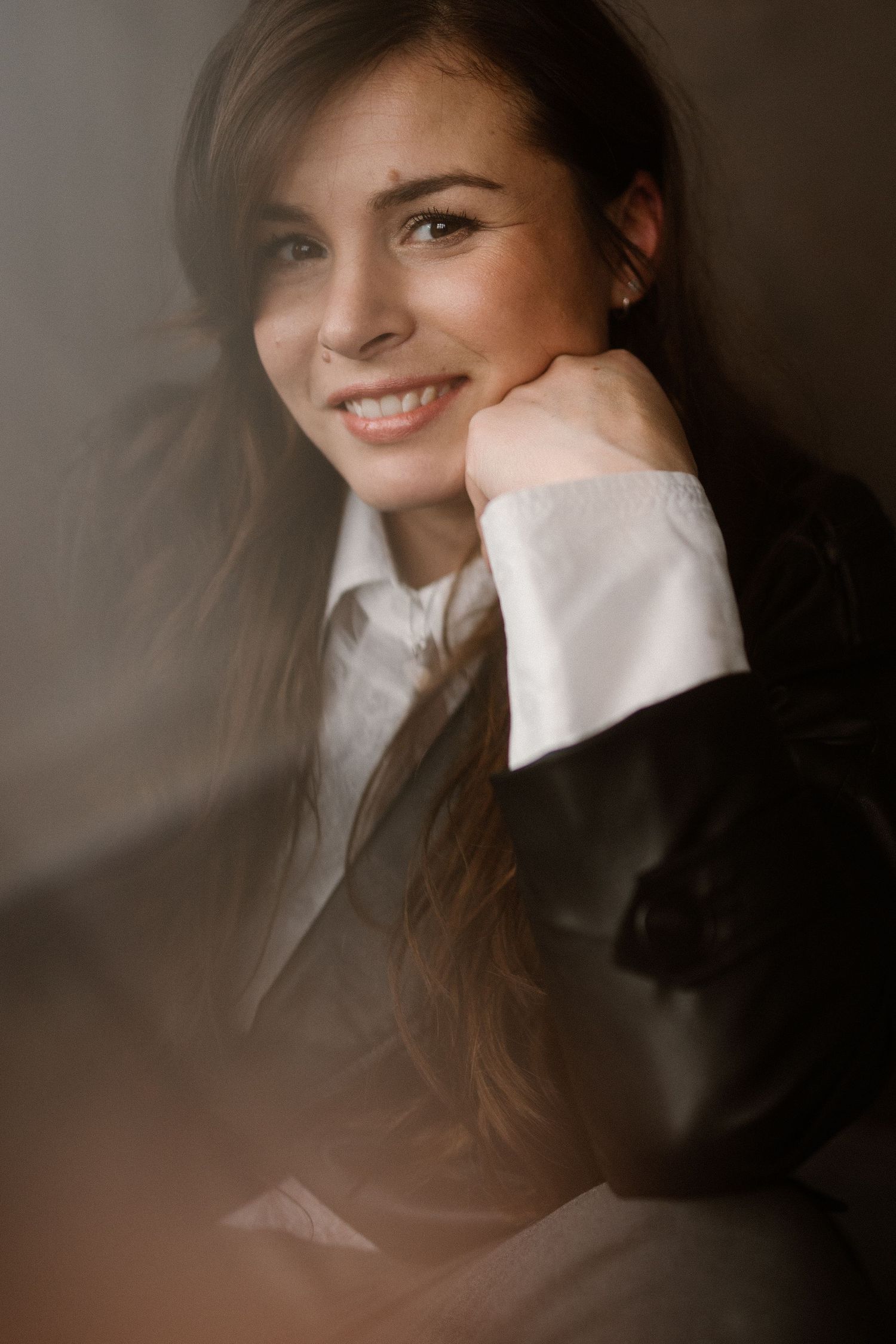 Professional portrait of a person in business attire smiling warmly while resting their chin on their hand.