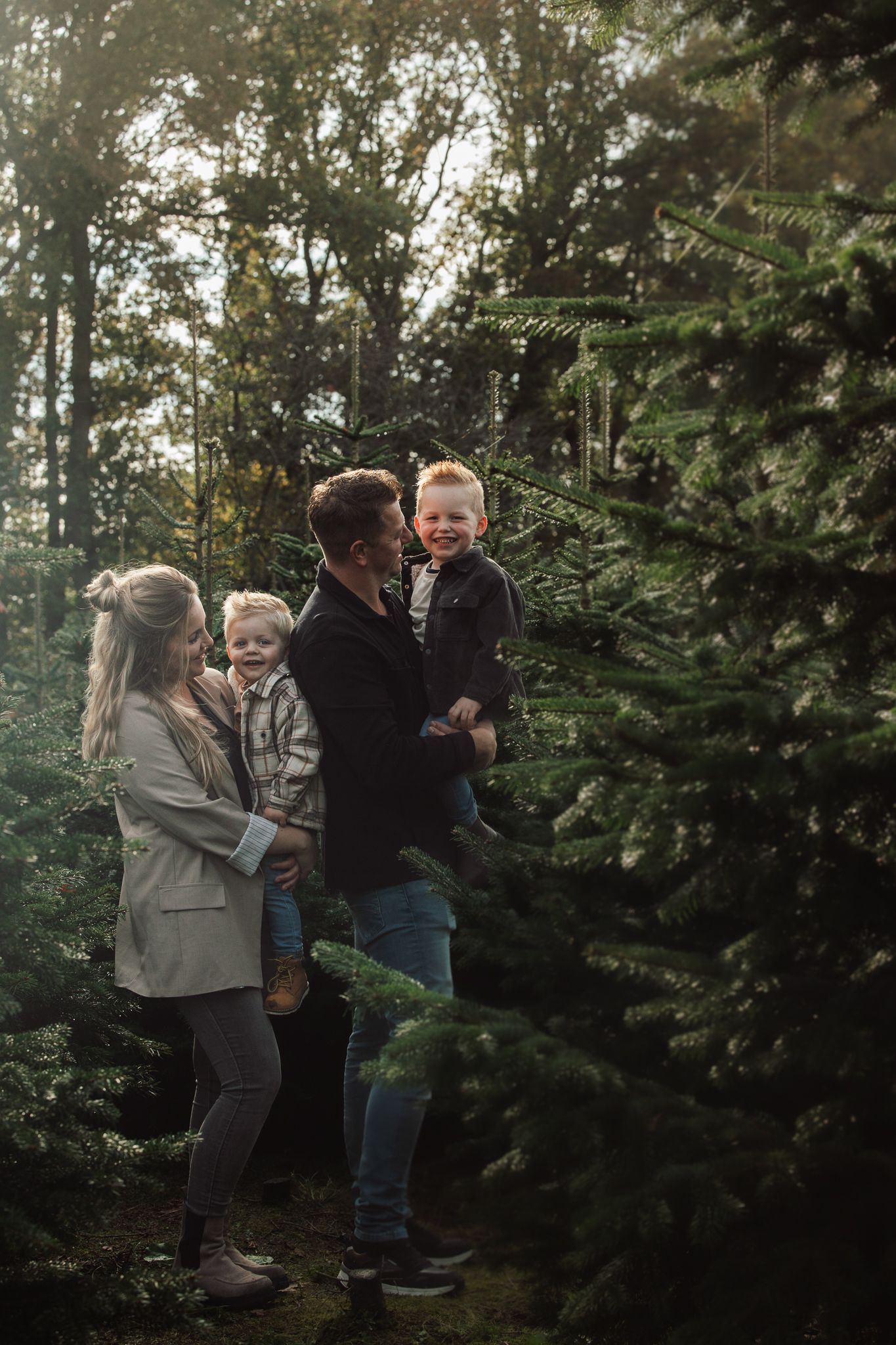 Family shares joyful moments among evergreen trees during outdoor photo session.