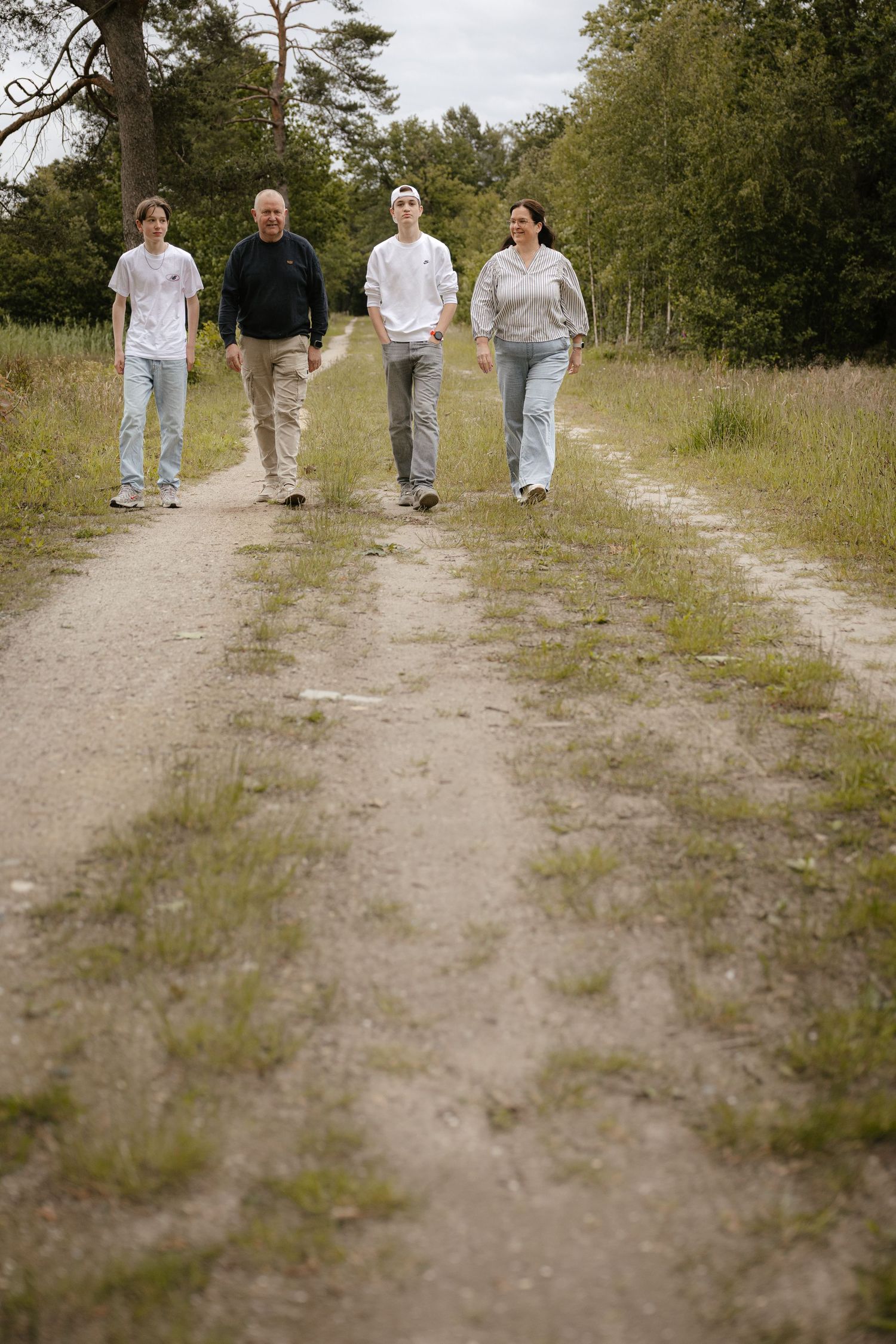 Family of four walking together on a dirt path through a scenic countryside landscape.
