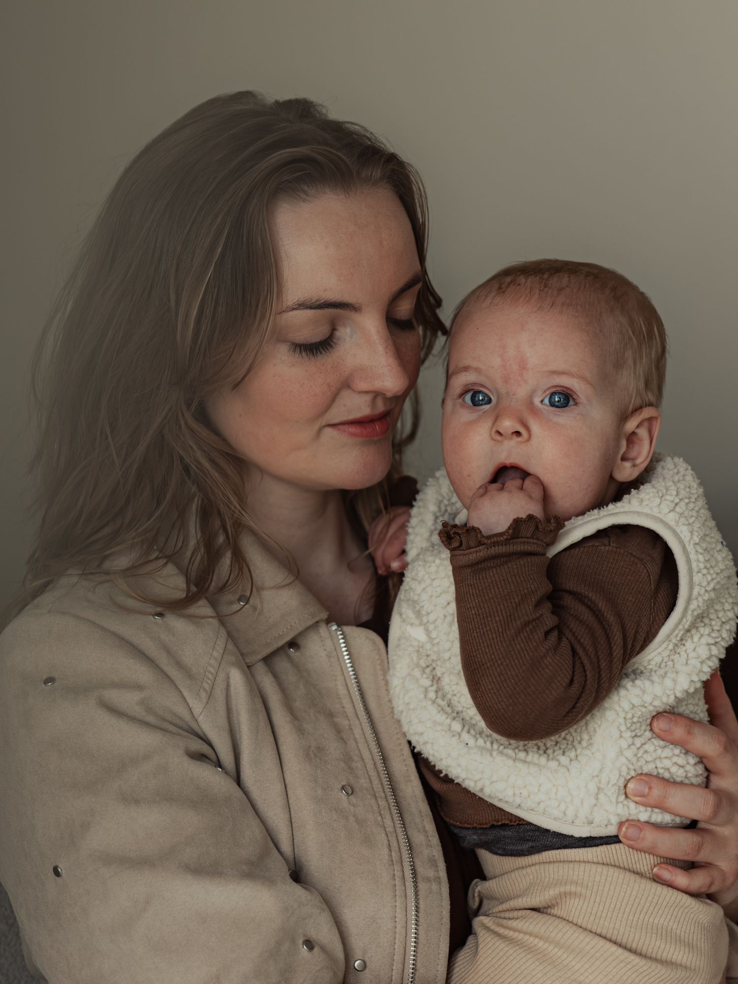 A woman with blonde hair holds a blue-eyed baby dressed in a brown and white sherpa outfit.
