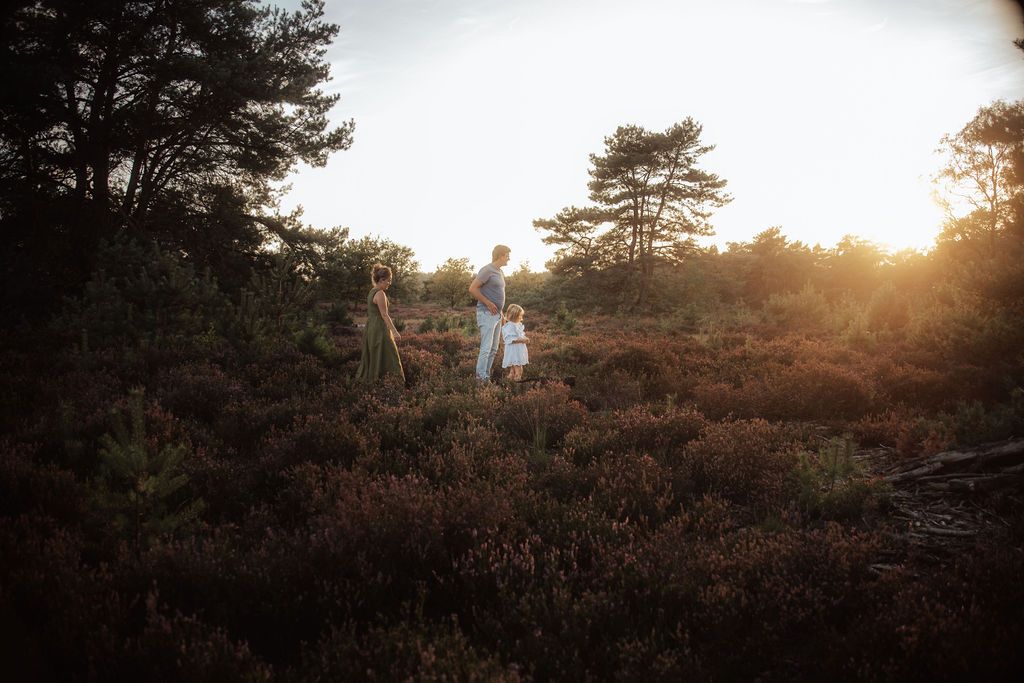Wide landscape shot of figures silhouetted against a setting sun on a heather-covered hill.