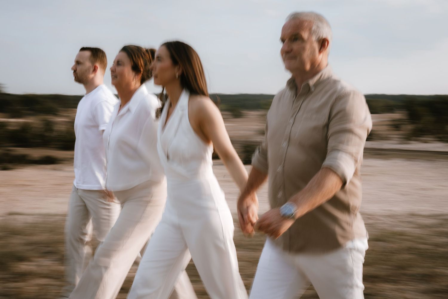 Four adults in white outfits walk together outdoors in a blurred motion photography style.