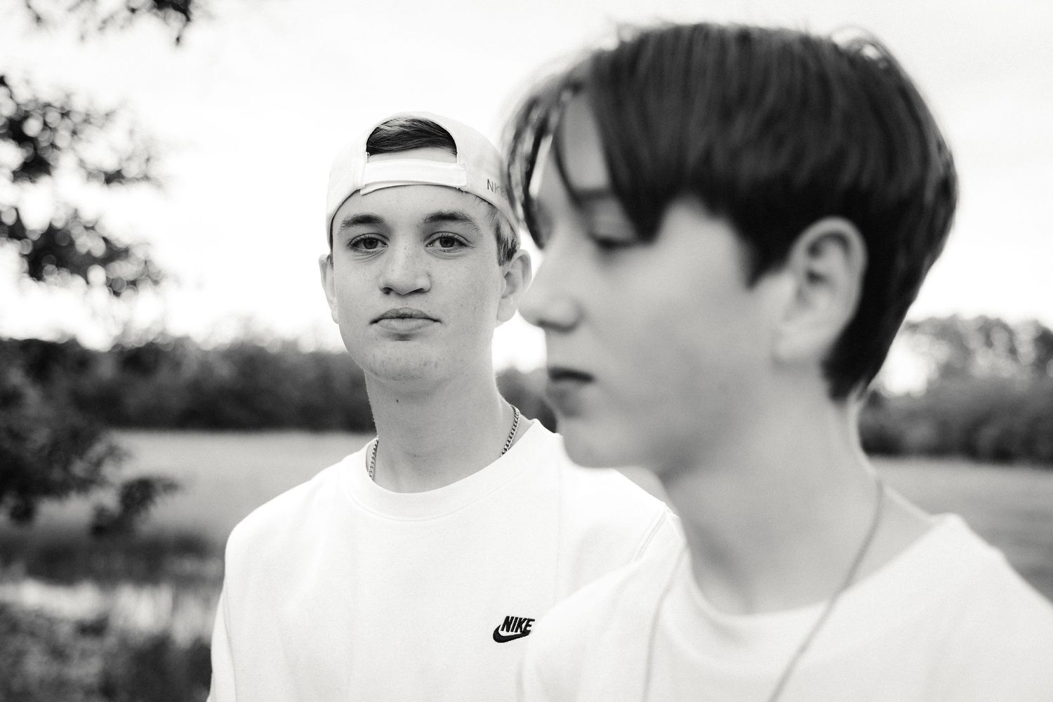 Two teenage boys in white Nike shirts outdoors, black and white photo, one wearing a backwards cap.