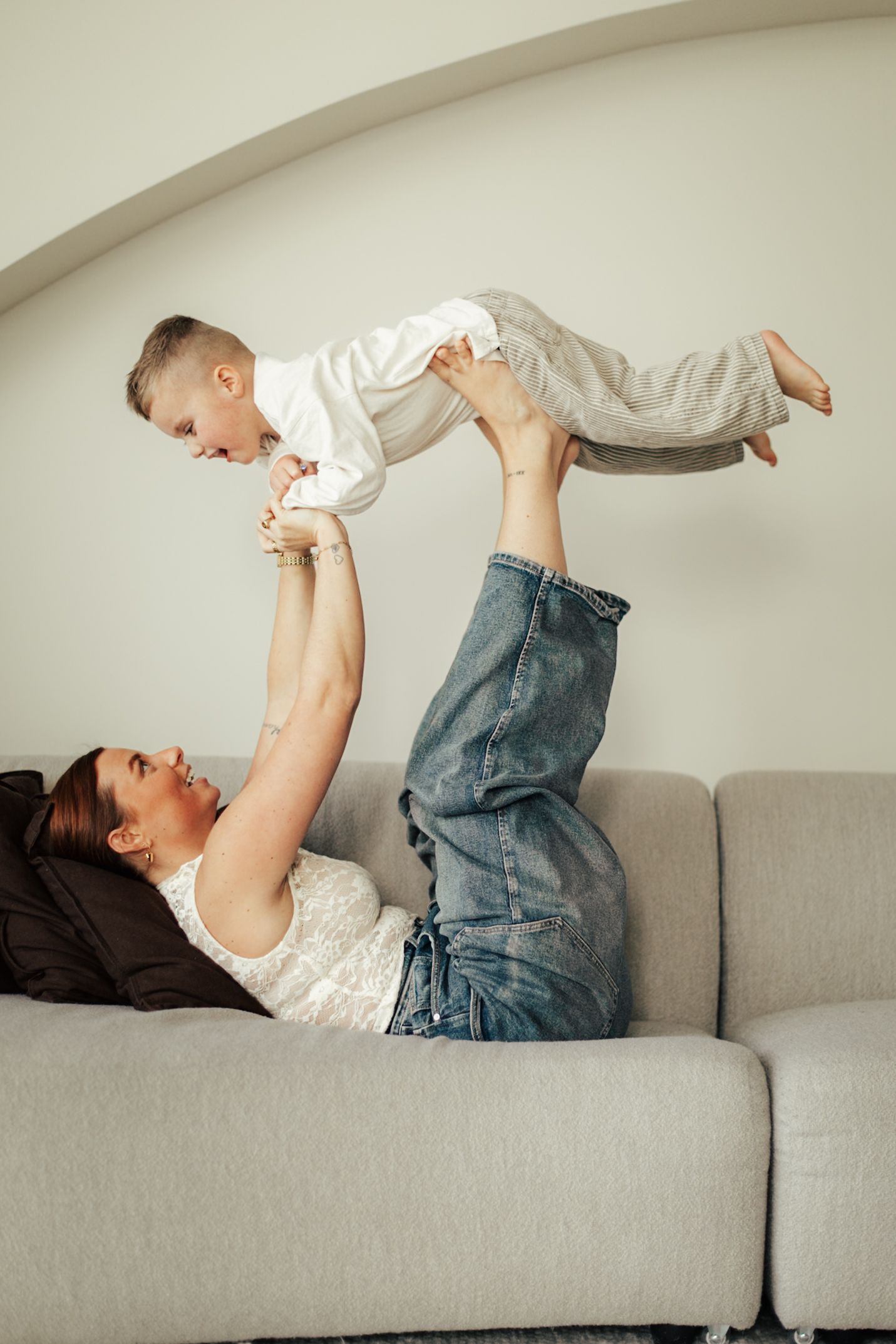 Playful moment on grey couch with parent lifting child in air.