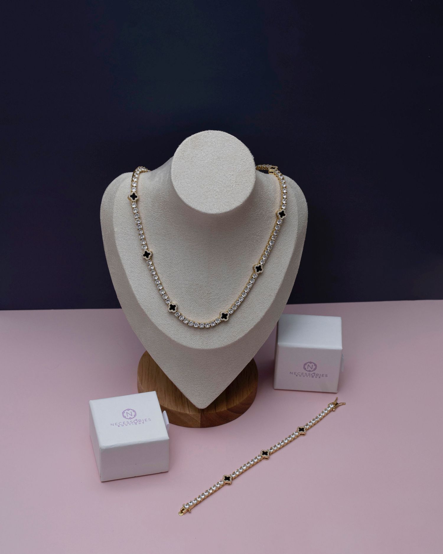 Gold and pearl beaded necklace and bracelet set displayed on white bust with jewelry boxes on pink surface.