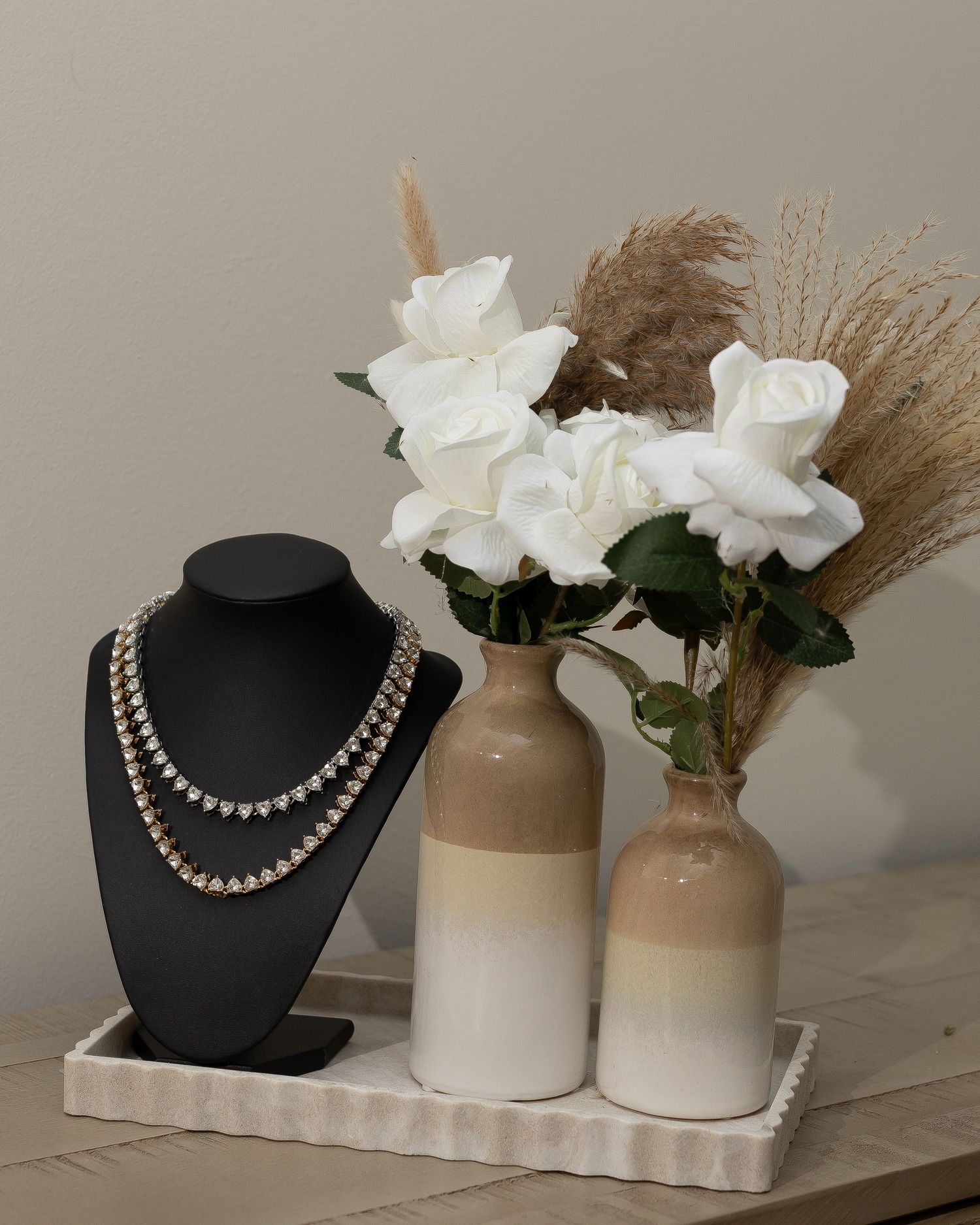 Elegant pearl necklaces displayed on black stands with white roses and neutral vases as decoration.