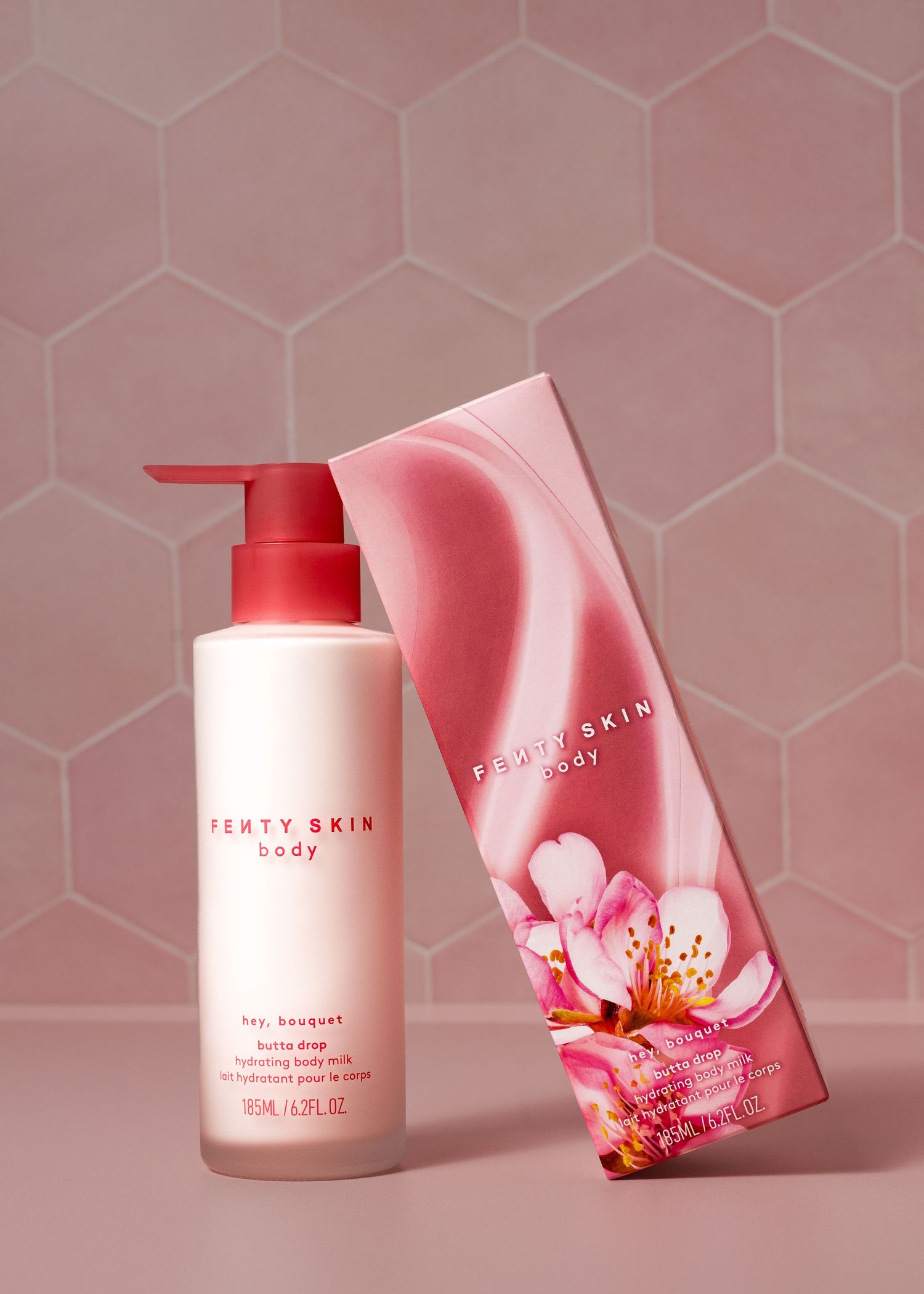 Fenty Skin Body Hey Bouquet hydrating body milk pump bottle with pink floral box on hexagon tile background.
