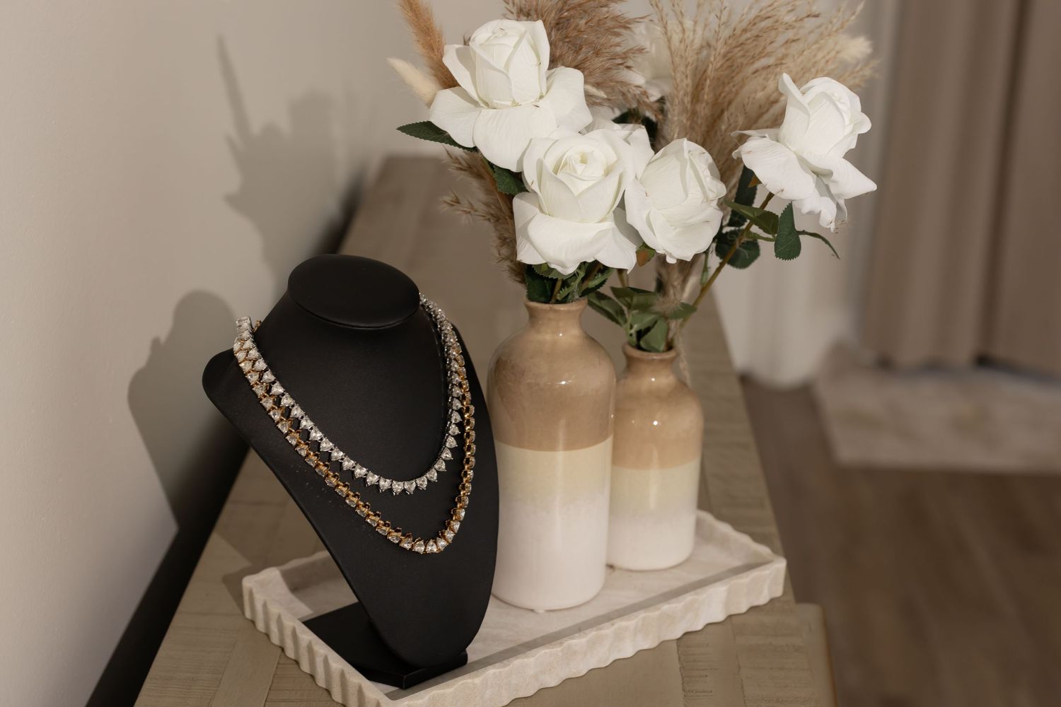 Elegant jewelry display featuring pearl necklaces with white roses and ceramic vases.