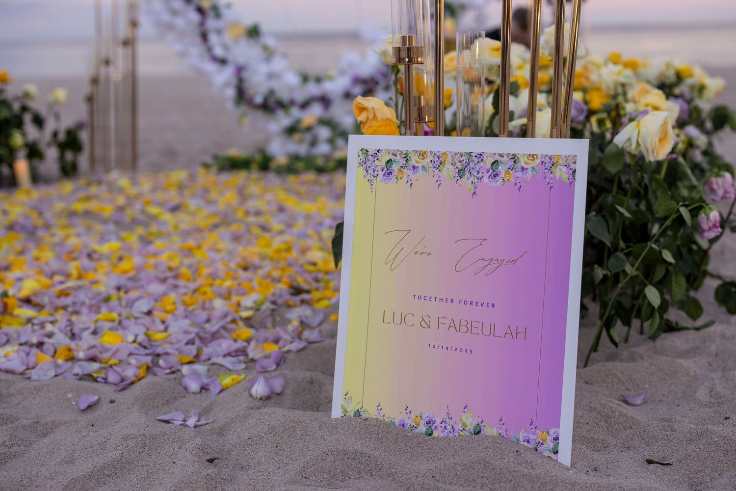 Wedding invitation cards scattered on sand with purple flower petals.