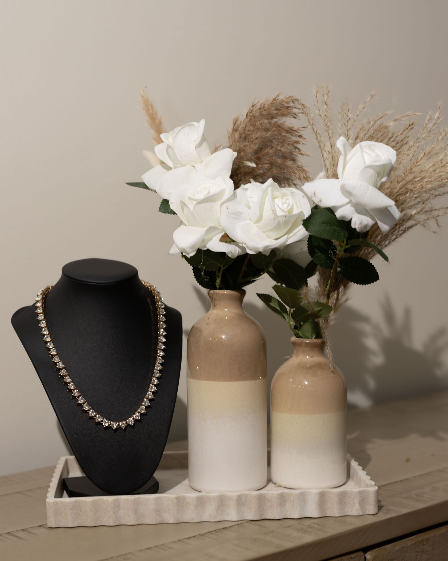 Elegant jewelry display featuring a black necklace bust with neutral vases and dried pampas grass decor on a shelf.
